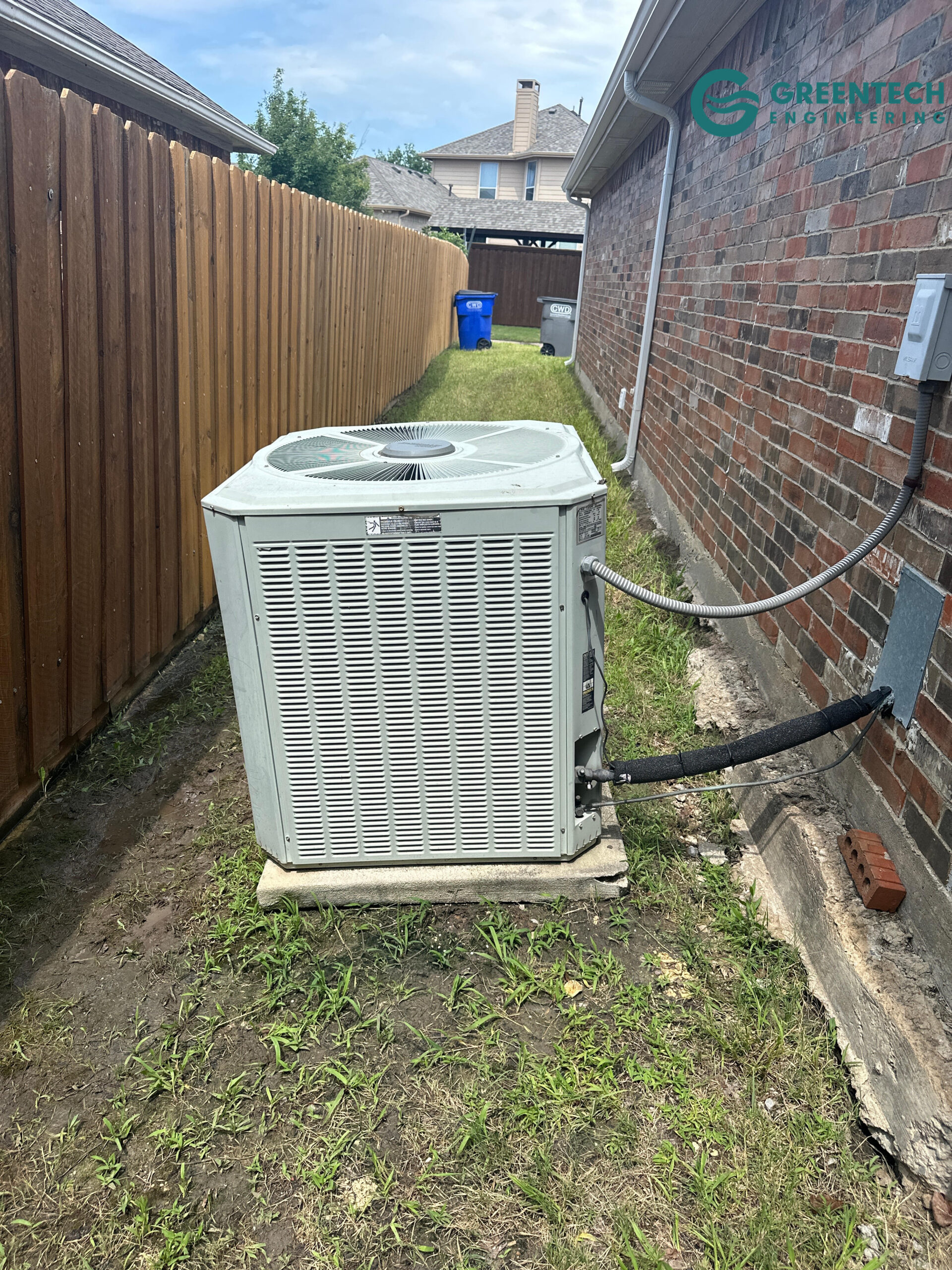 An old, inefficient Trane air conditioning condenser unit sitting outside a brick house.