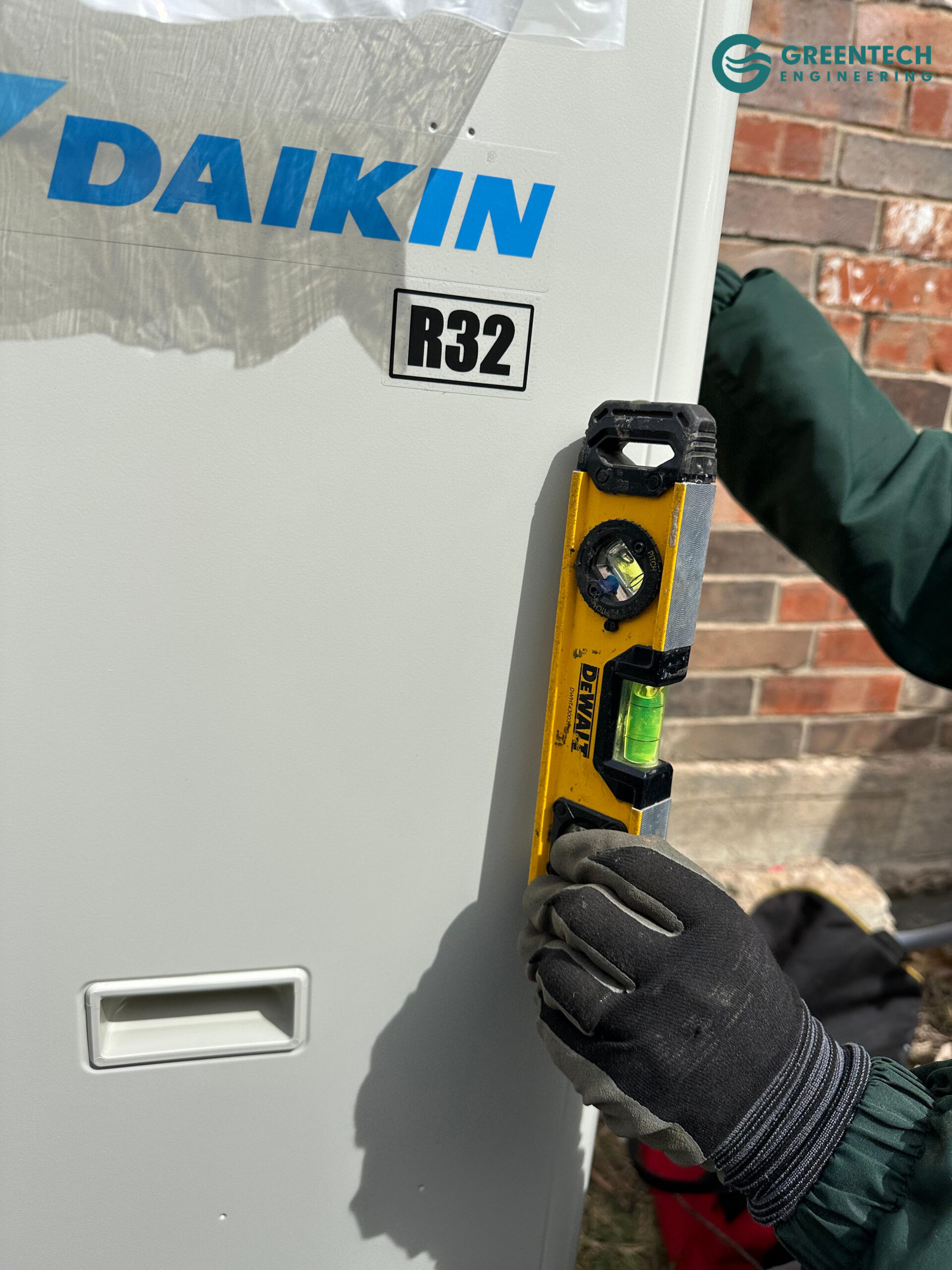 Technician using a yellow DeWalt level on a new Daikin R32 heat pump condenser.