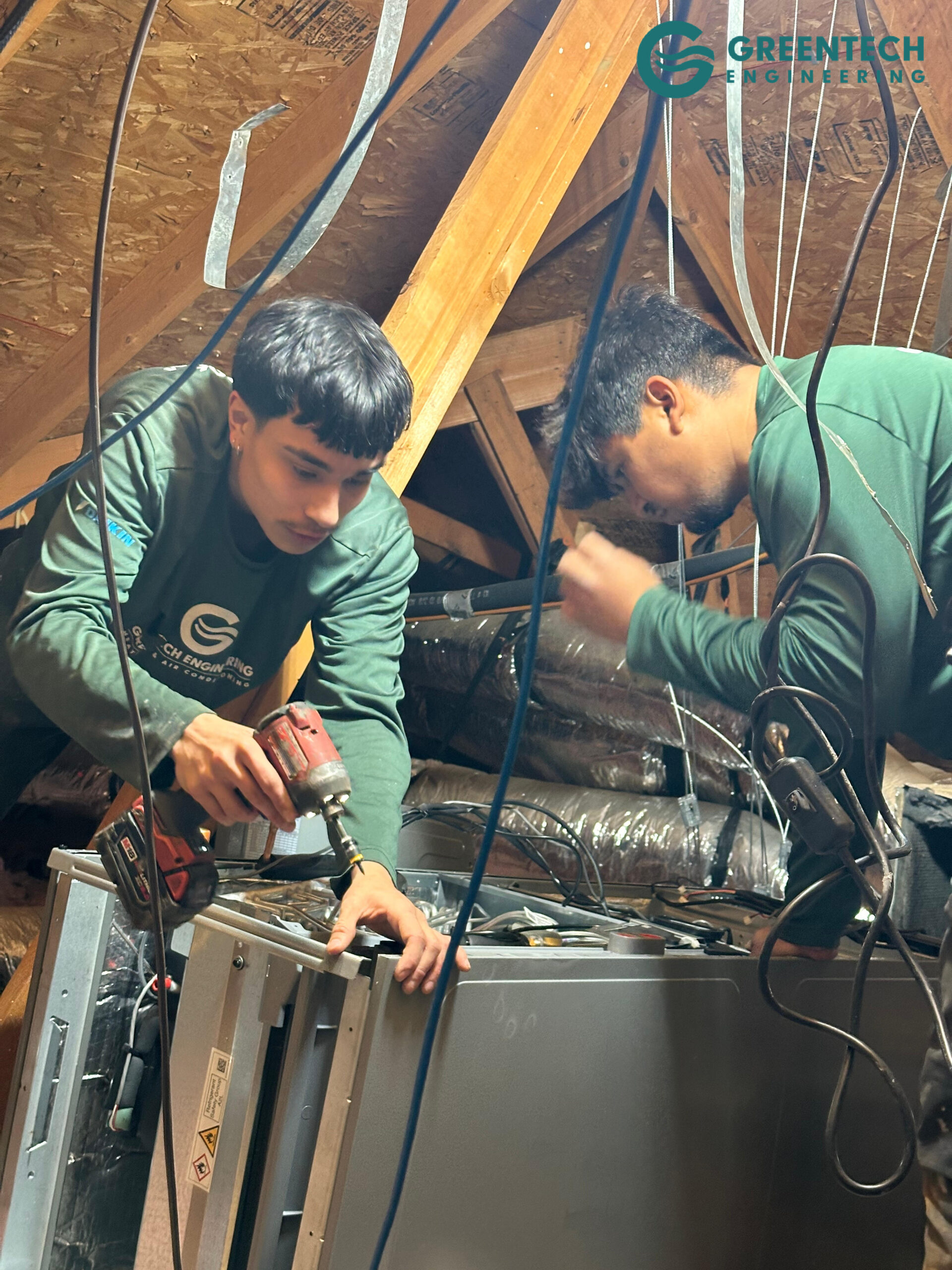 Two Greentech Engineering technicians installing a new HVAC indoor unit in an attic.