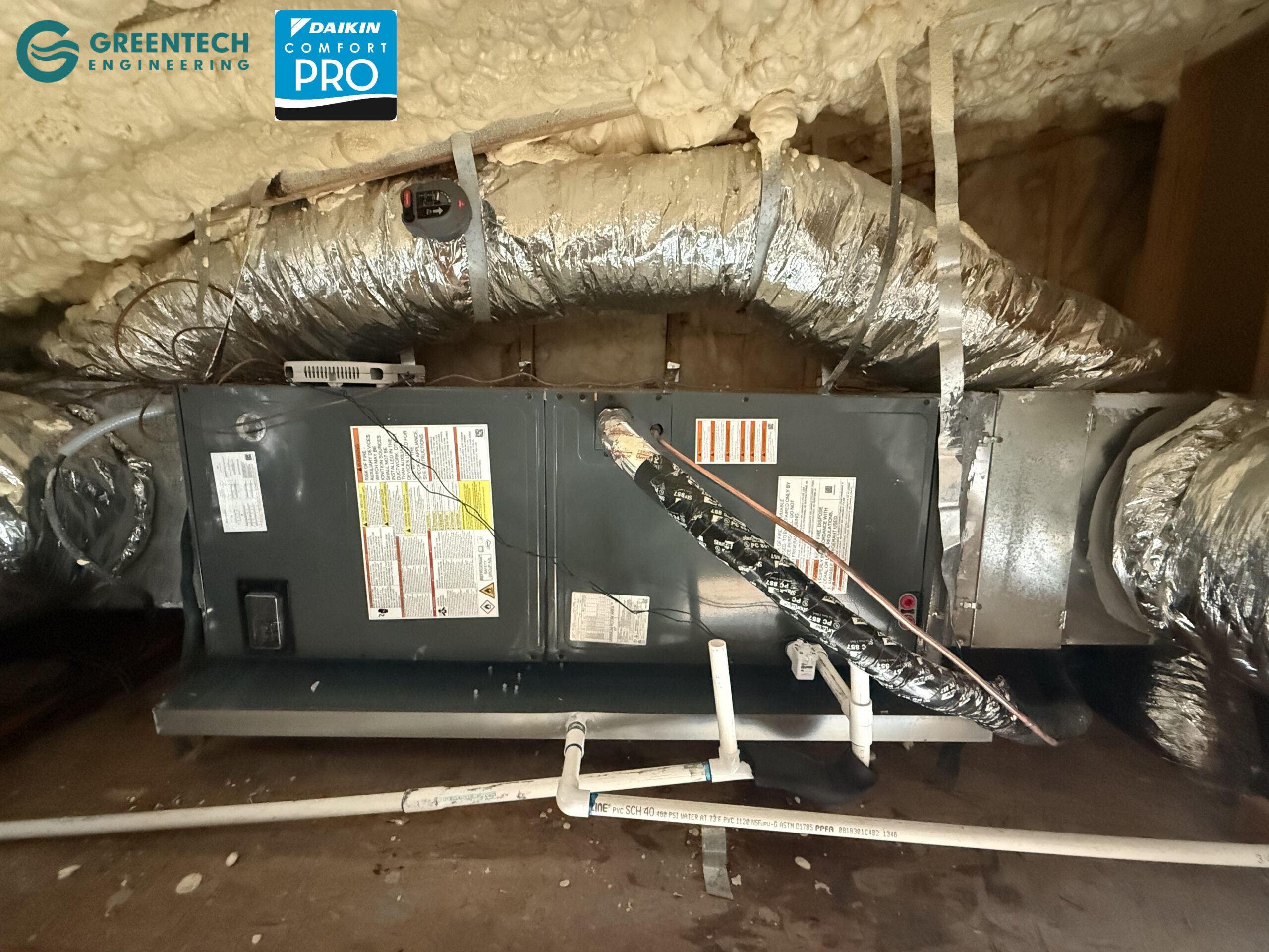 A newly installed, highly efficient Goodman air handler suspended in a spray-foamed Dallas residential attic, featuring a hard-piped PVC drain and emergency safety switch.