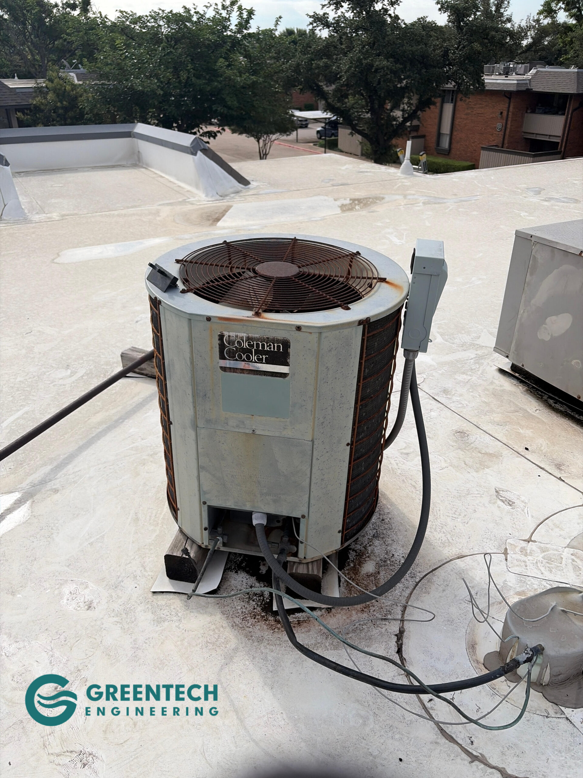 An aging, rusted Coleman air conditioning condenser sitting on a flat apartment rooftop in Dallas, Texas 75248.
