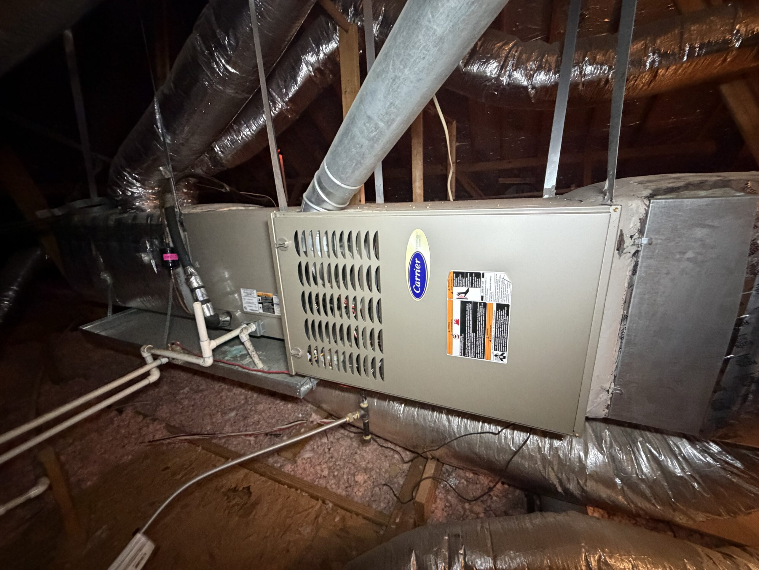 An older, inefficient Carrier indoor furnace and coil system with failing ductwork connections suspended in a Dallas, TX attic.