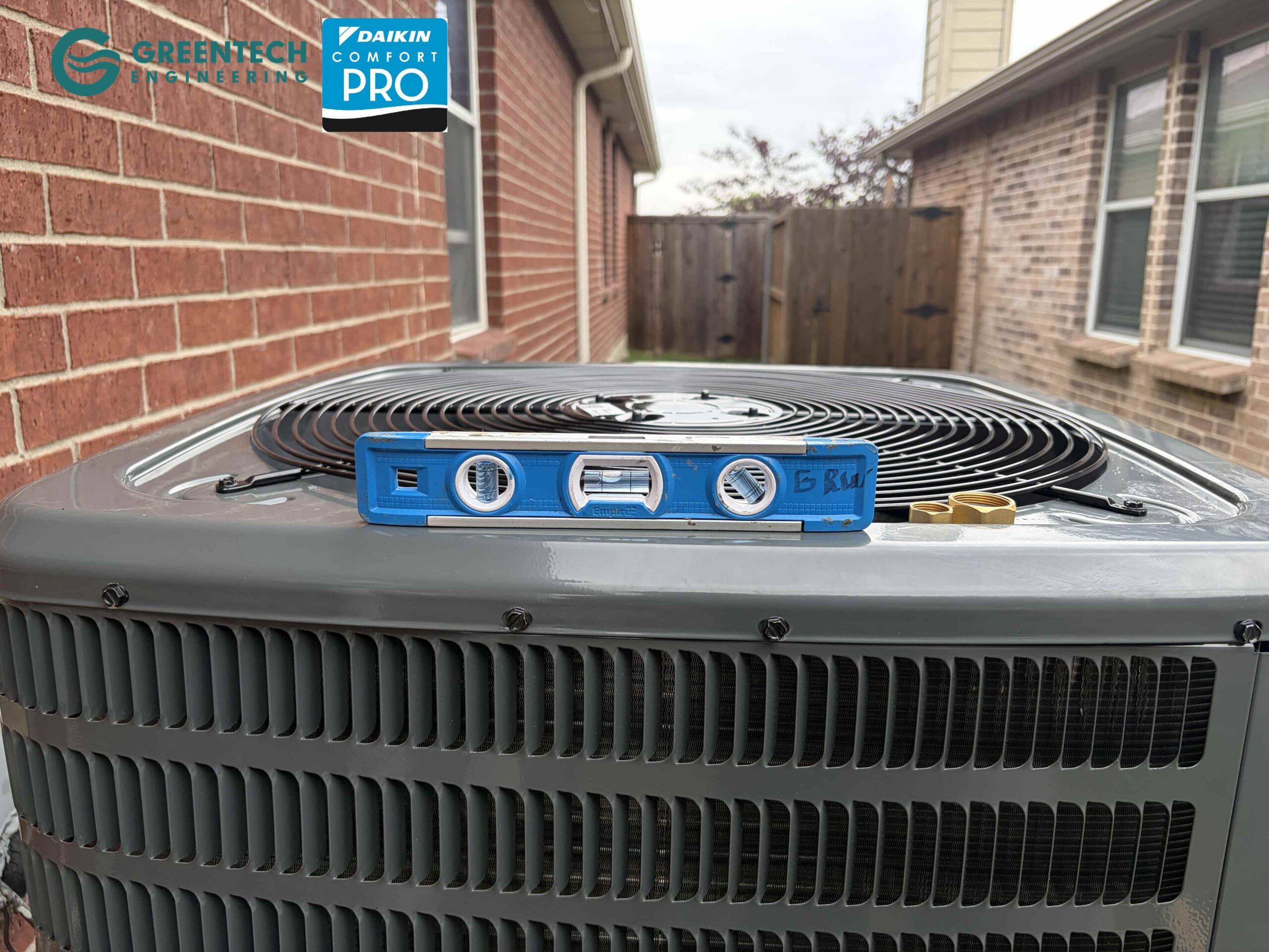 A blue torpedo level sitting on top of the newly installed Goodman air conditioning condenser to ensure perfect balance on the concrete pad.