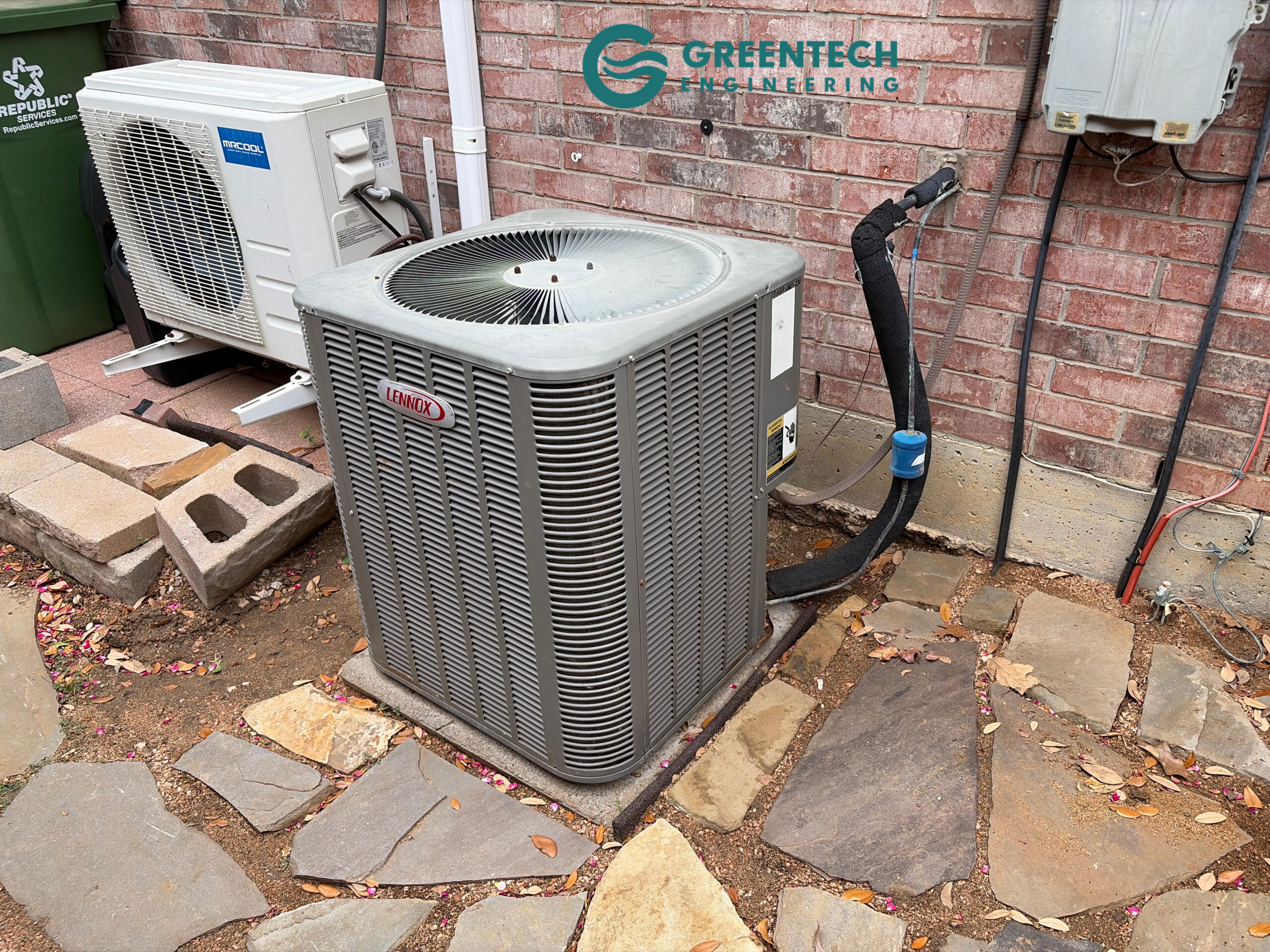 An aging, oversized 5-Ton Lennox air conditioning condenser sitting on a stone pathway outside a brick Dallas home.