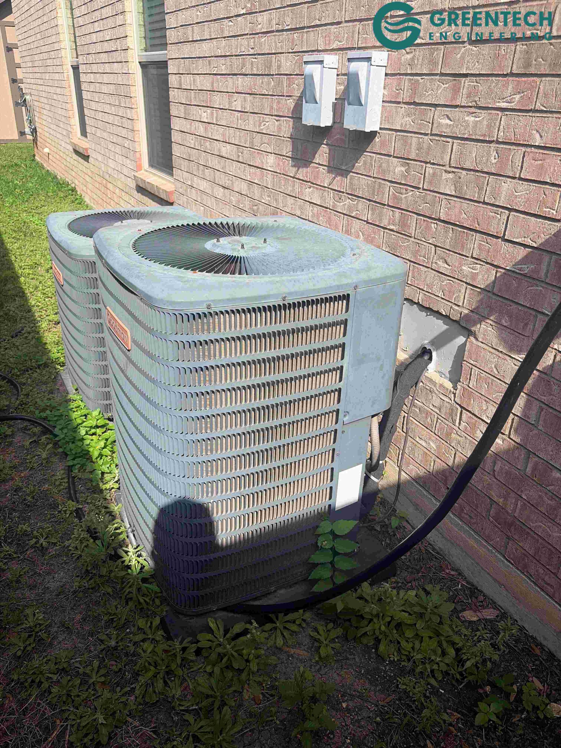 Two aging, oversized Goodman air conditioning condensers sitting outside a brick single-family home in Fort Worth, Texas 76177.