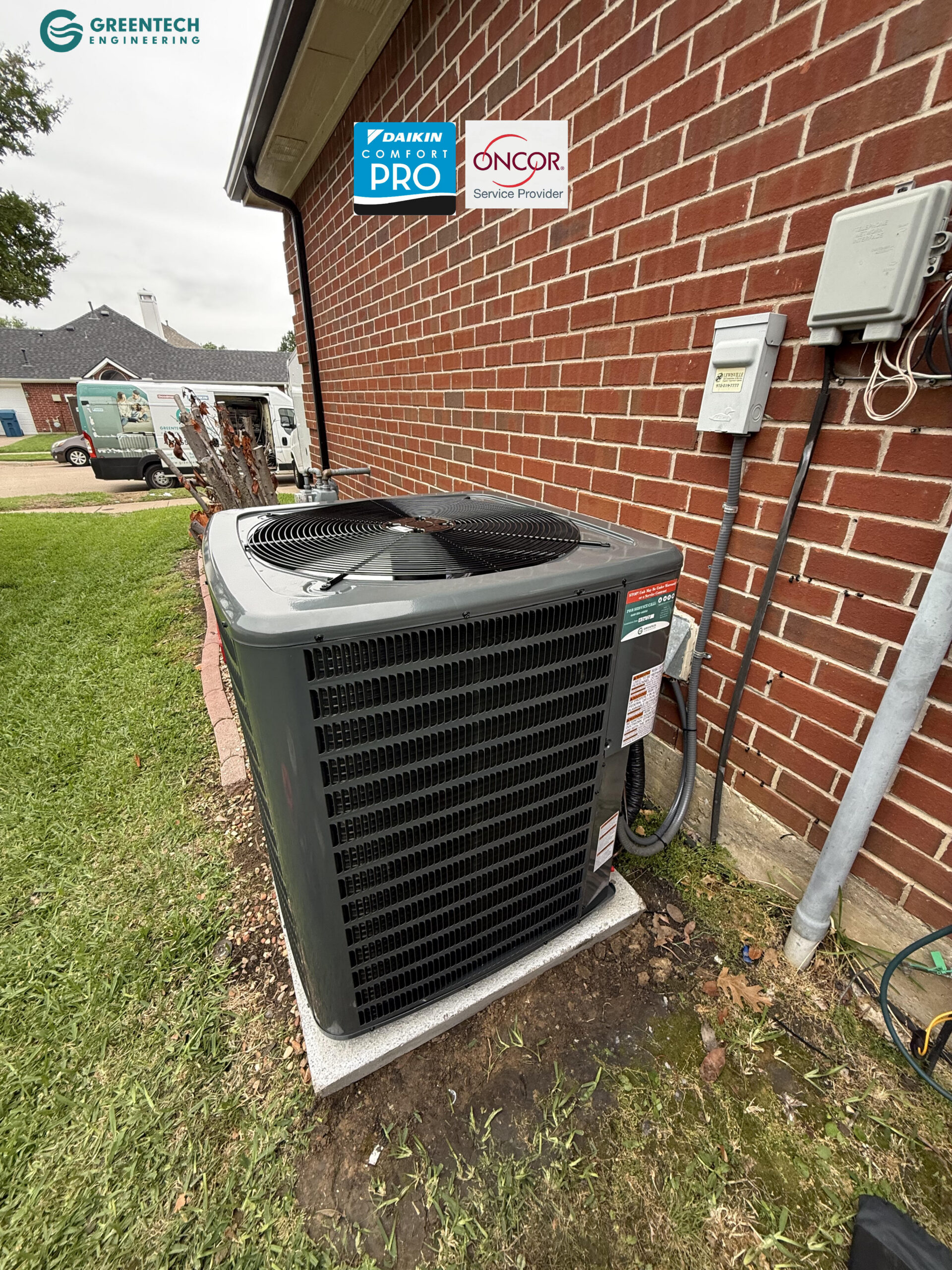 A brand new, dark grey Goodman air conditioning condenser installed cleanly on a level pad beside a brick house.