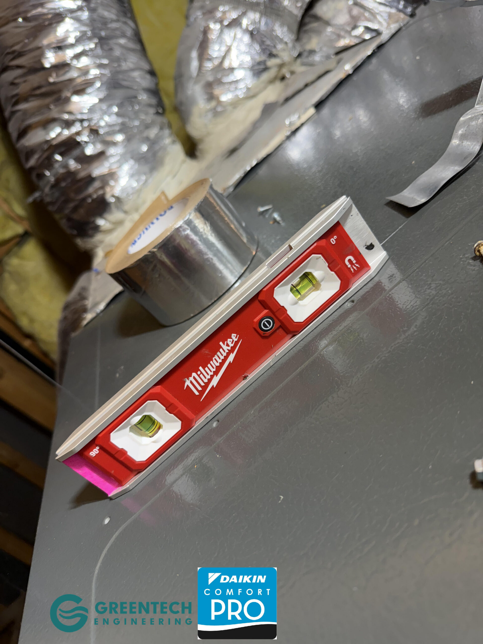 A red Milwaukee magnetic level resting on a newly installed grey HVAC furnace cabinet in an attic to ensure perfect horizontal alignment.
