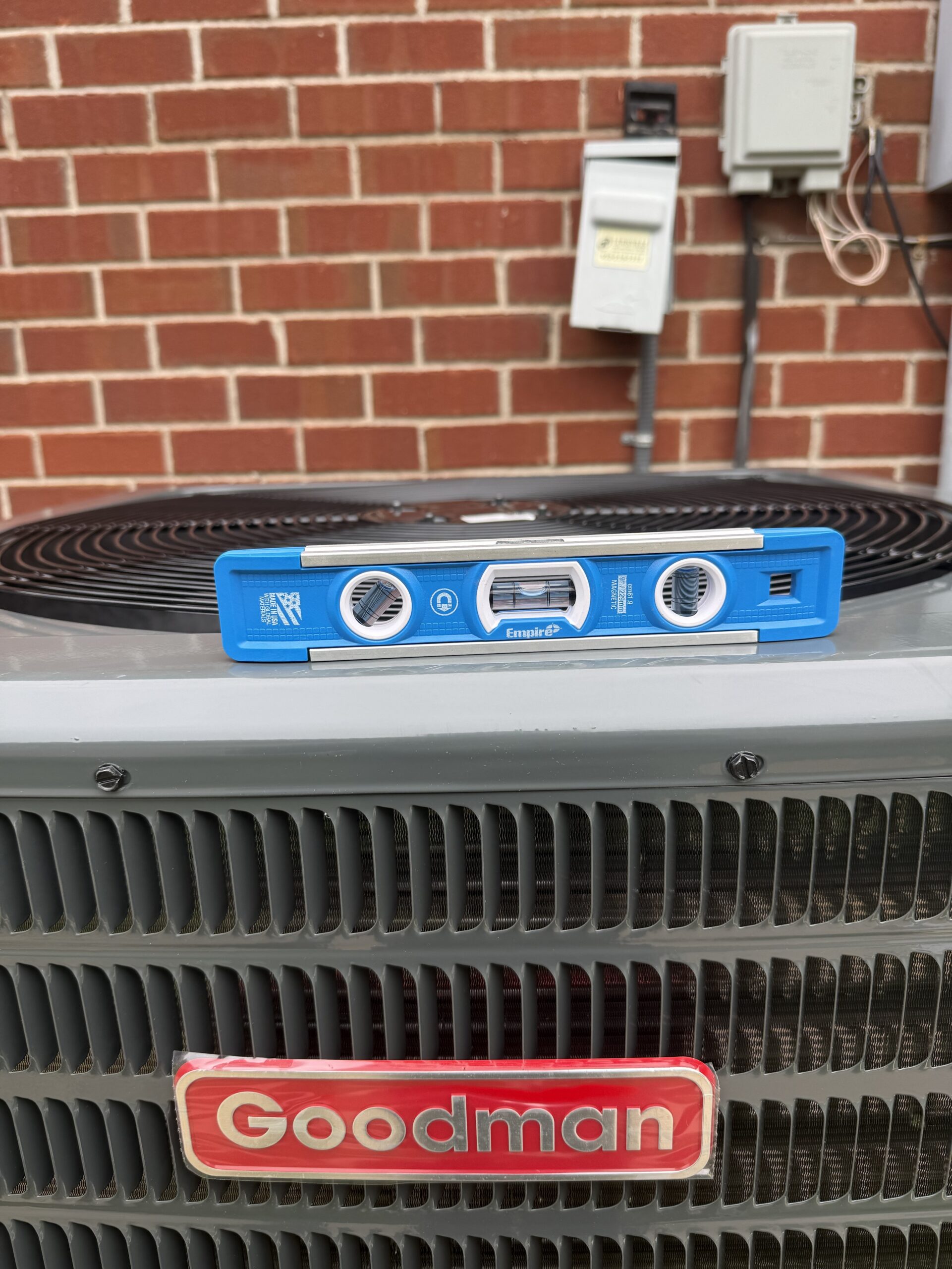 A blue Empire level resting on the fan grate of a newly installed Goodman air conditioning condenser.