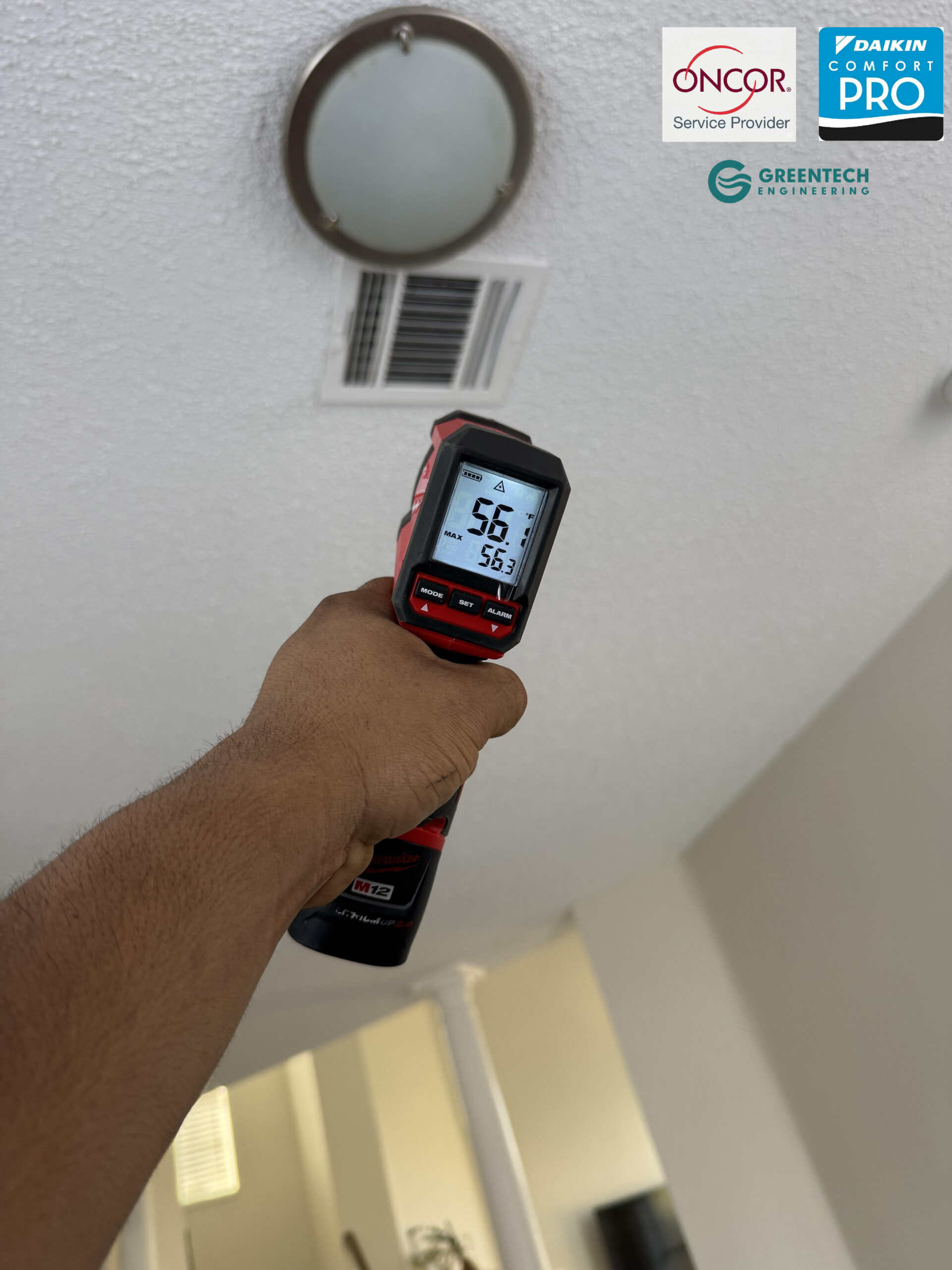 HVAC technician verifying 56-degree supply air temperature from a ceiling register after new AC installation.
