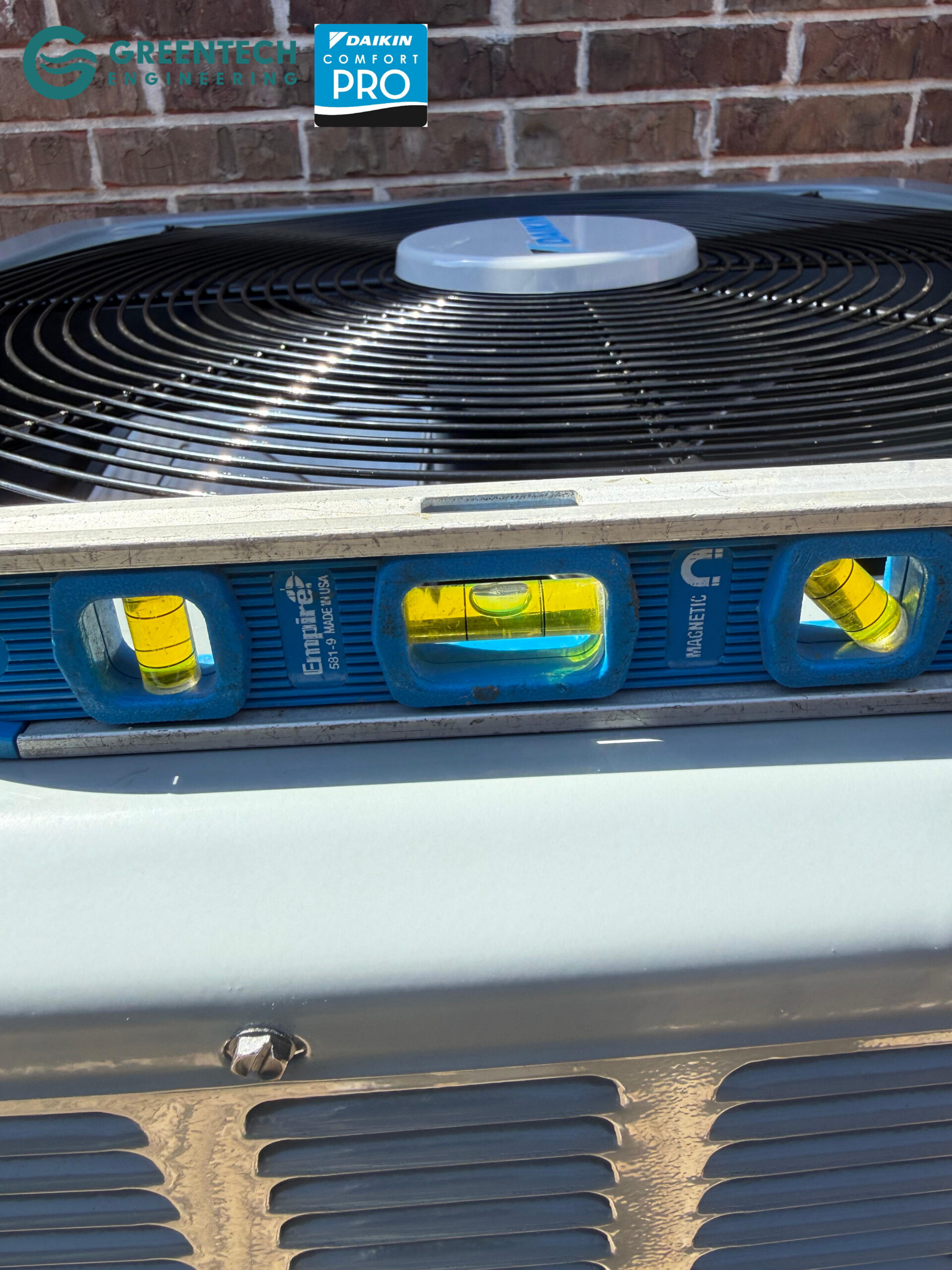 A precision spirit level sitting on top of a newly installed Daikin AC condenser to ensure perfect balance on a concrete pad.
