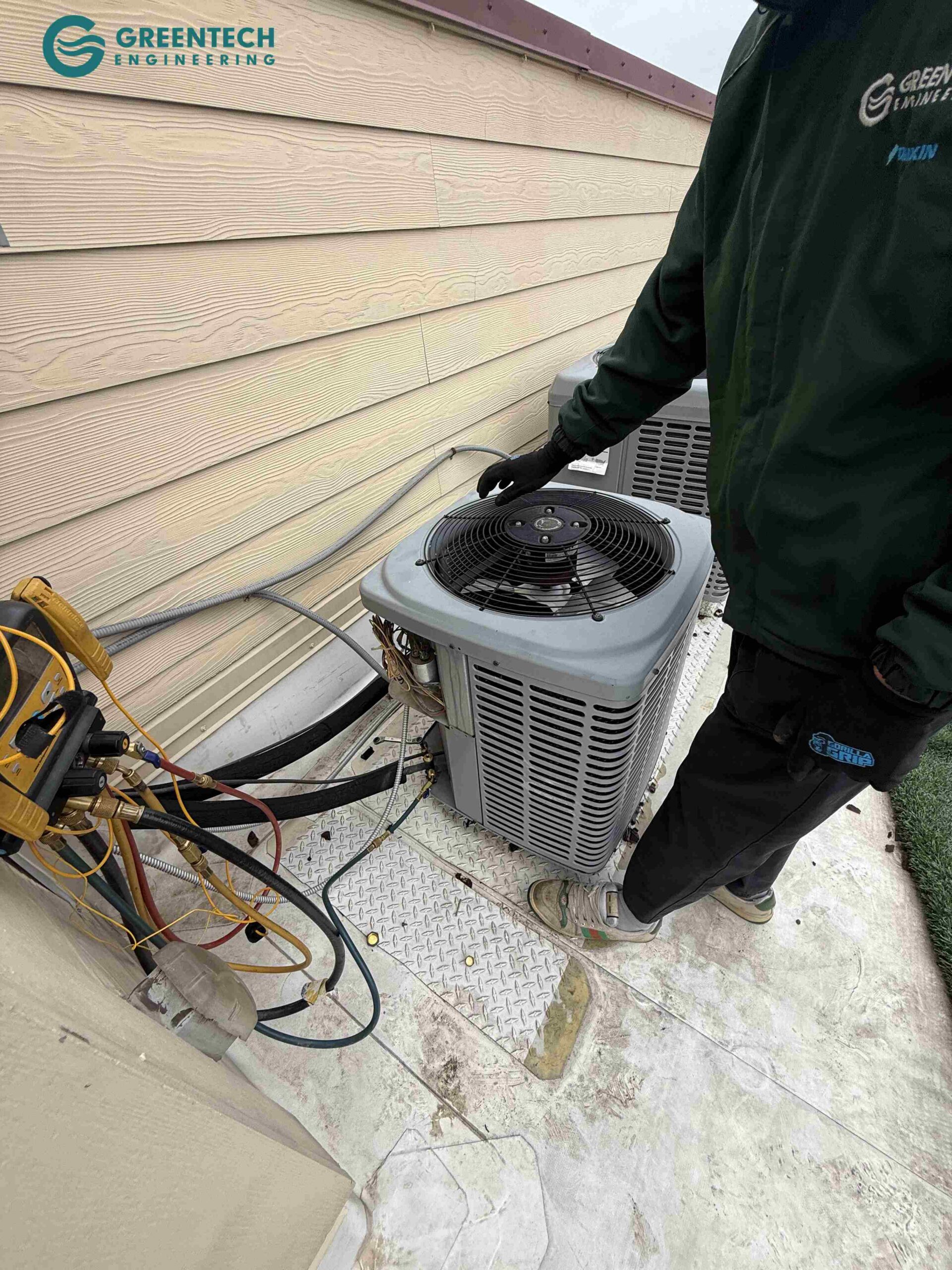 A Greentech Engineering technician in a uniform evaluating an old, inefficient York air conditioning condenser outside a home in Dallas 75248.