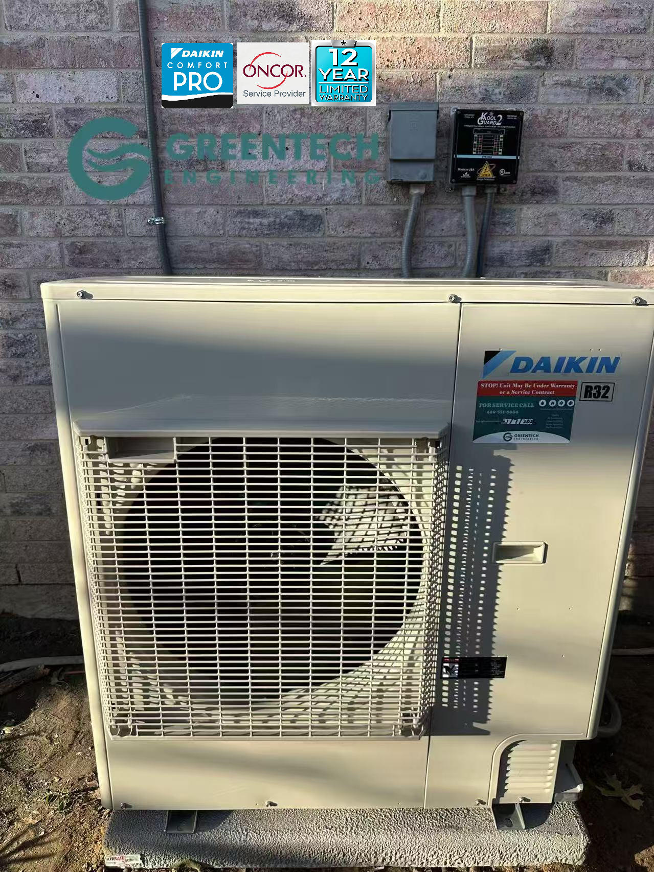 A slim, side-discharge Daikin Fit variable-speed heat pump condenser installed on a concrete pad outside a brick home by Greentech Engineering
