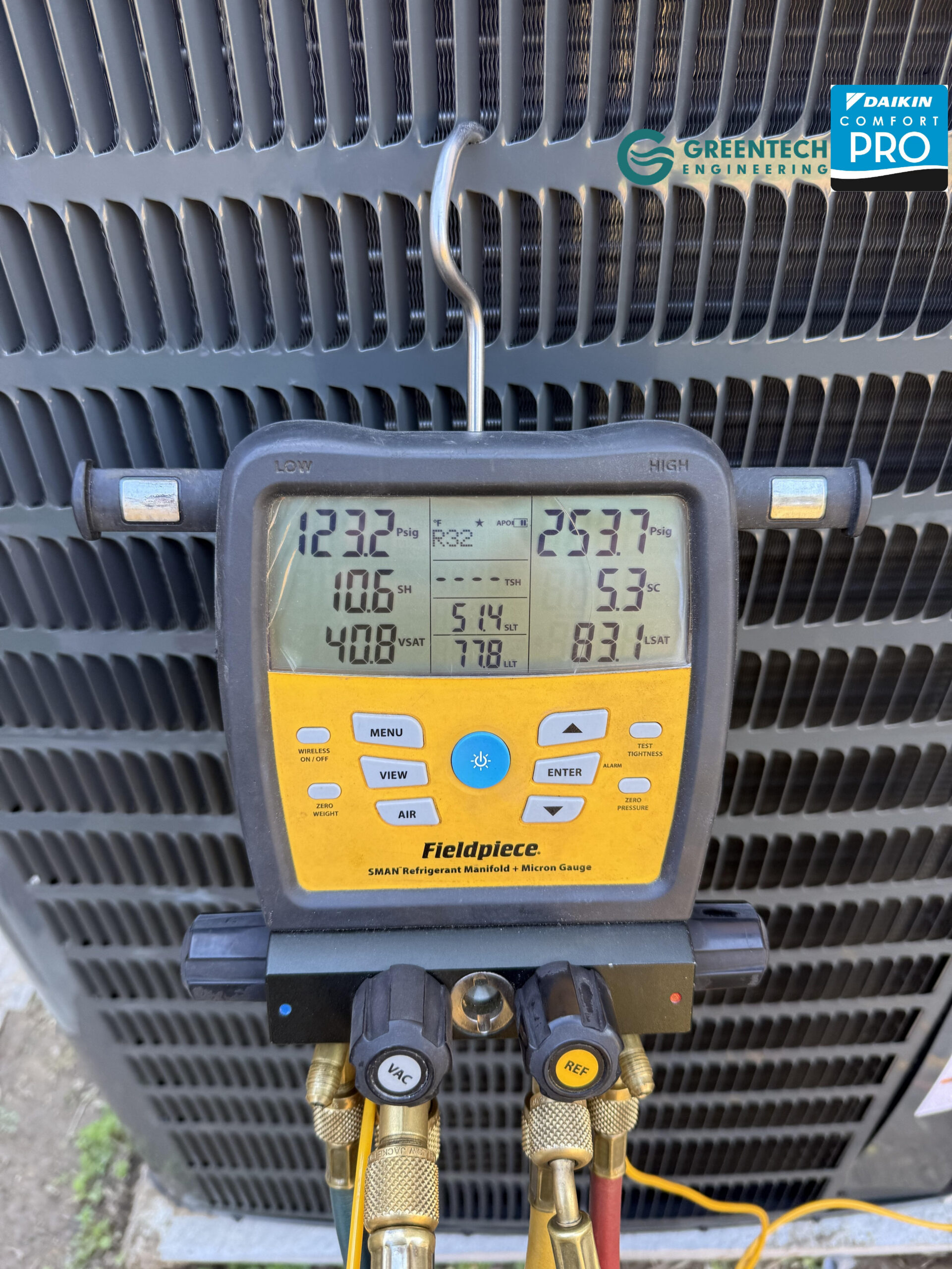 Greentech technician using digital yellow Fieldpiece gauges to test an AC condenser’s refrigerant pressure.