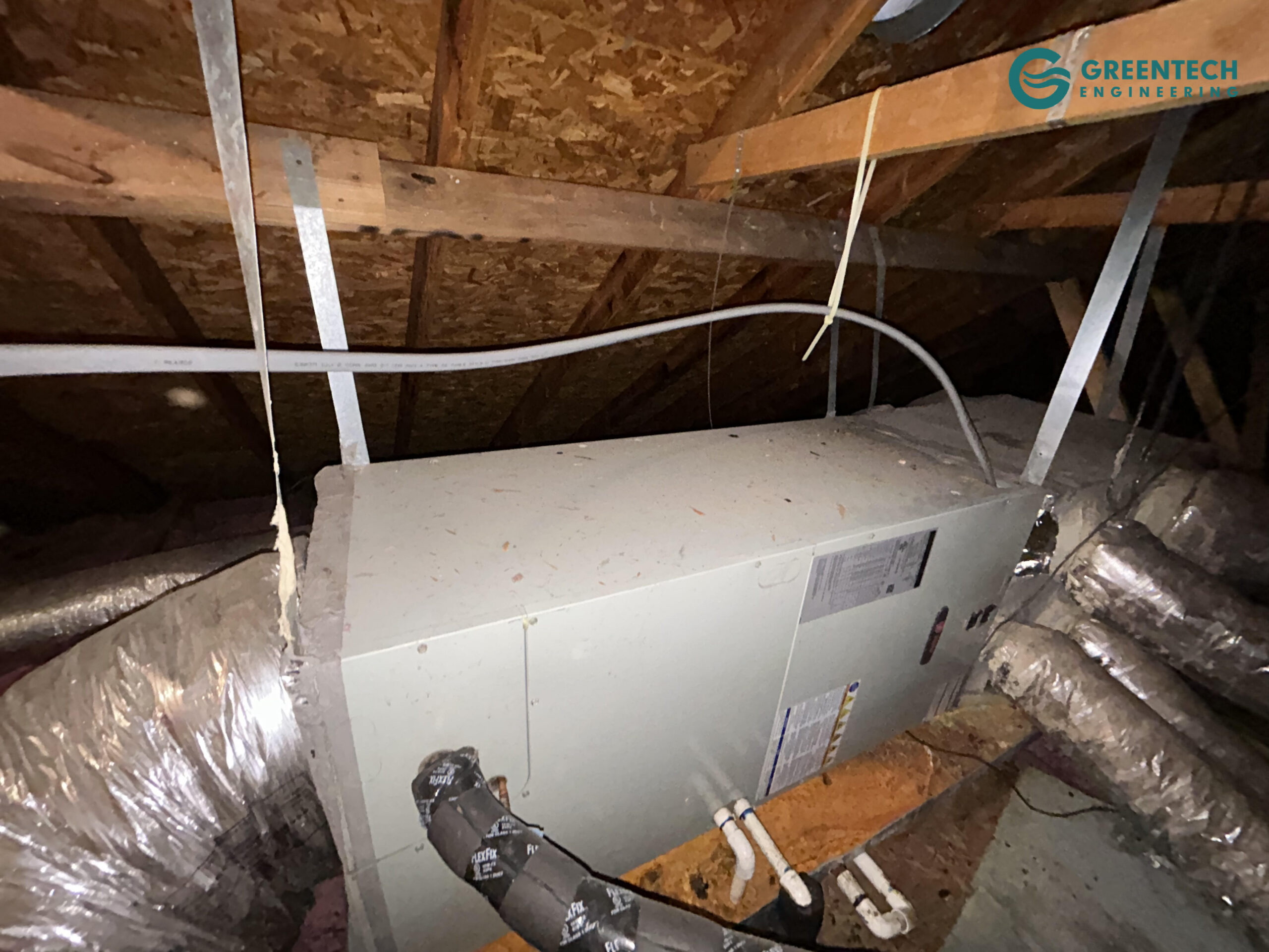 Old Trane gas furnace and coil installed in a dark attic.