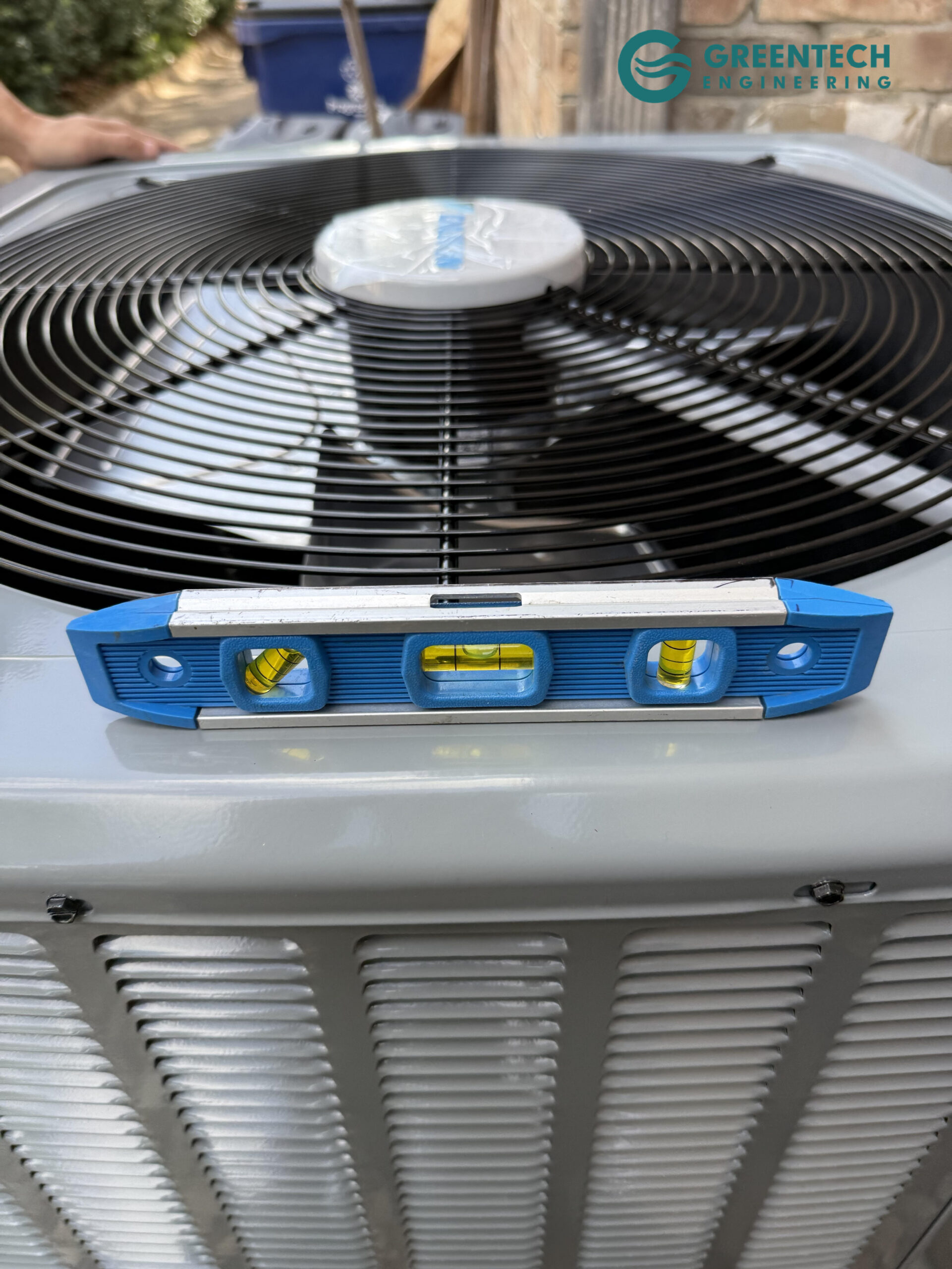 A blue magnetic spirit level resting on top of a newly installed Daikin condenser fan guard, showing the unit is perfectly balanced.