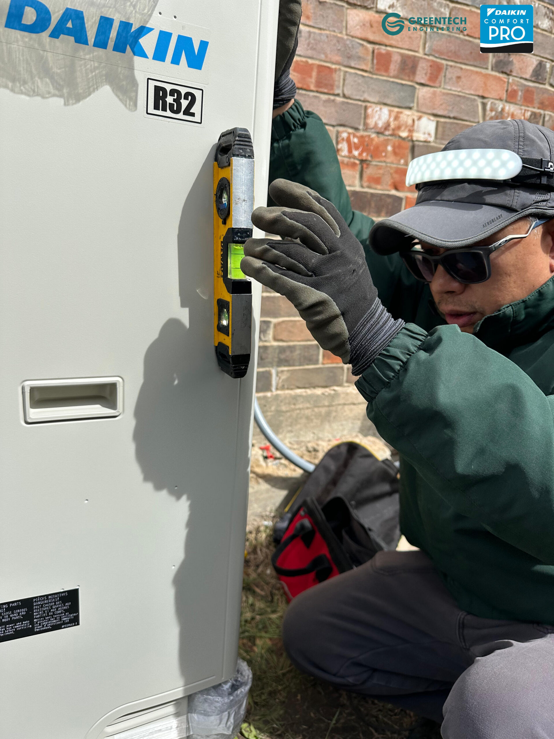 An HVAC technician using a yellow DeWalt torpedo level to ensure the newly installed Daikin Fit side-discharge condenser is perfectly balanced.