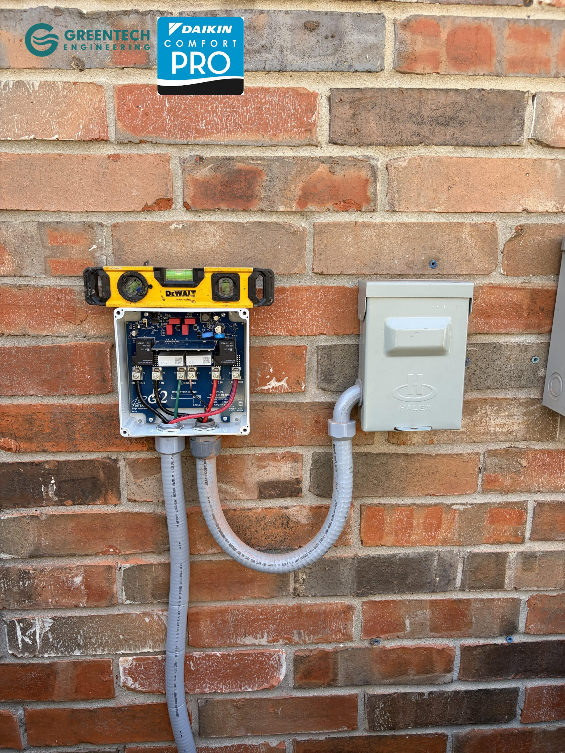 A newly installed 220V electrical disconnect and Kool Guard surge protector mounted on a brick wall, perfectly leveled by Greentech Engineering.