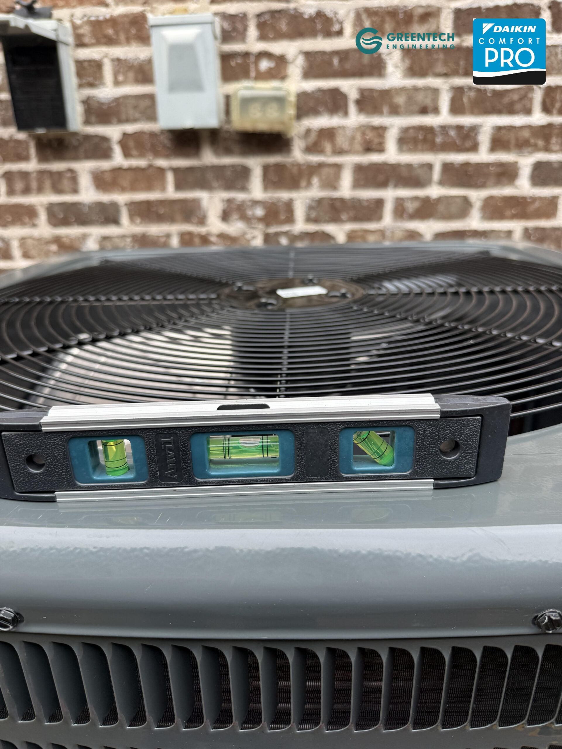 A precision spirit level sitting on top of a newly installed Goodman heat pump condenser to ensure perfect balance on a concrete pad.