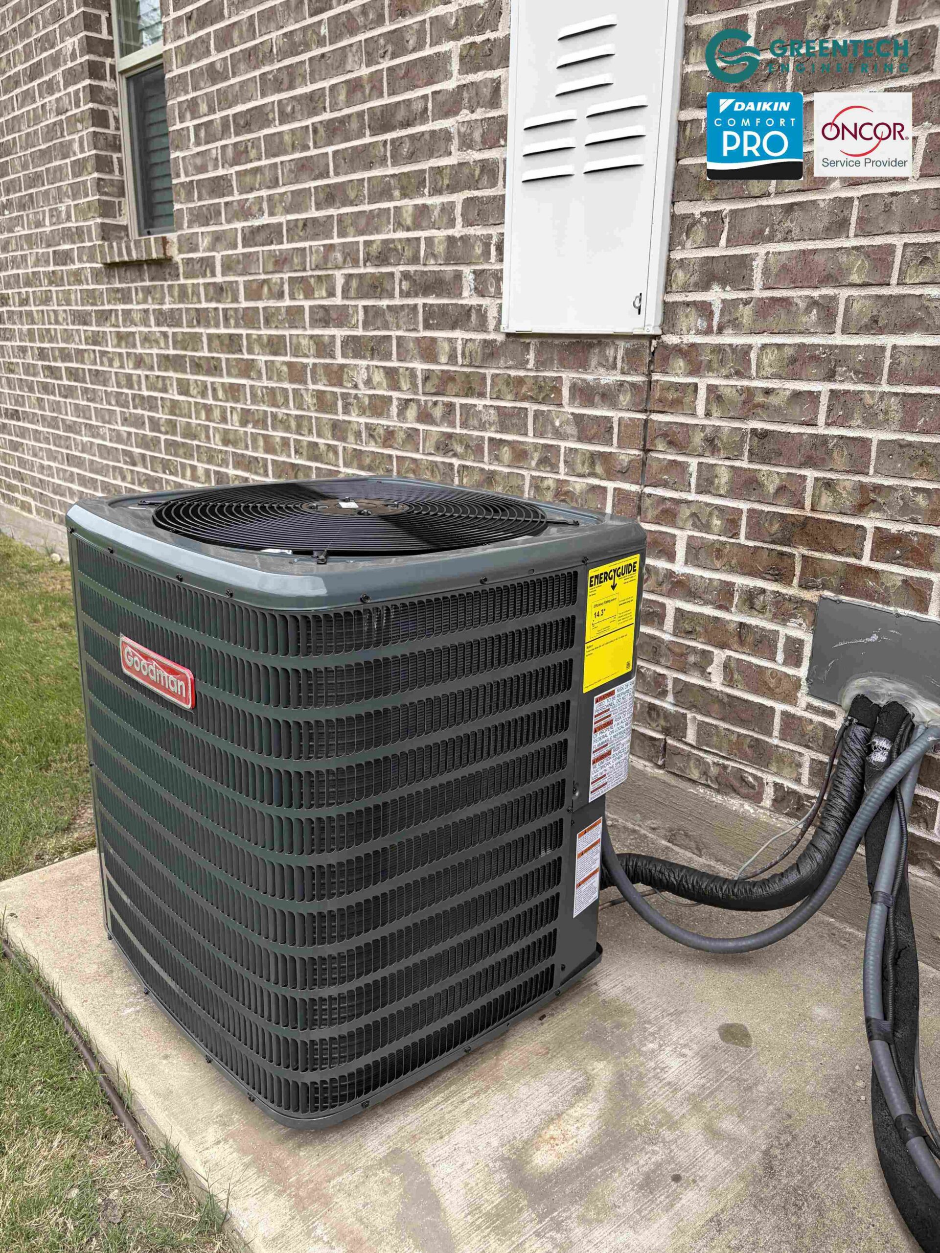 A brand new, dark grey Goodman air conditioning condenser installed cleanly on a leveled concrete pad next to a brick house in Dallas.