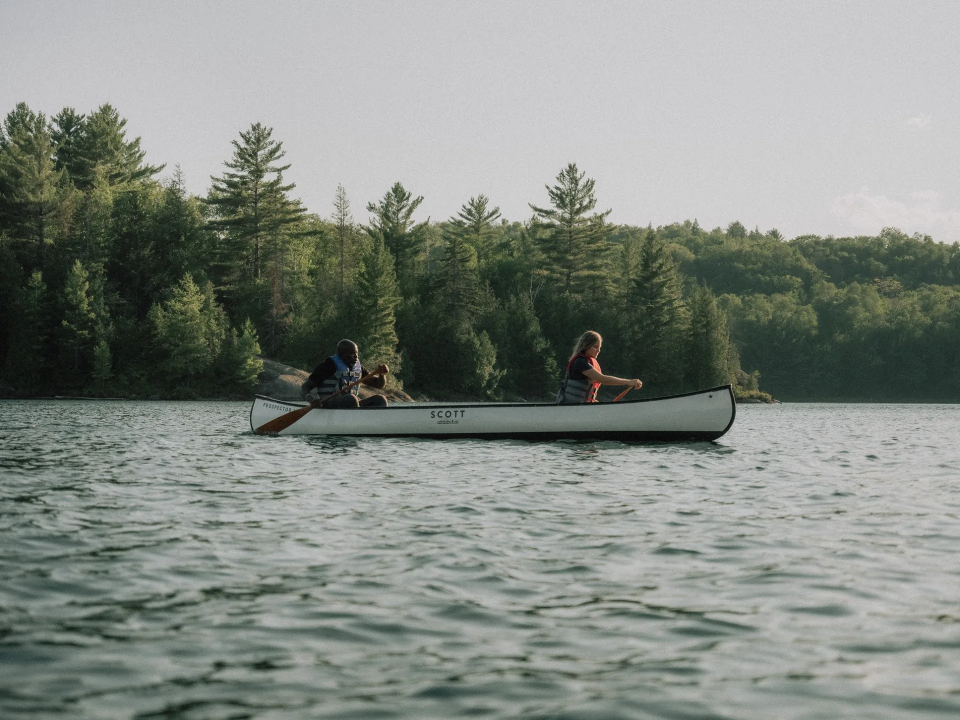 Deux personnes pagayant en canot sur un lac calme entouré de forêt dans Lanaudière