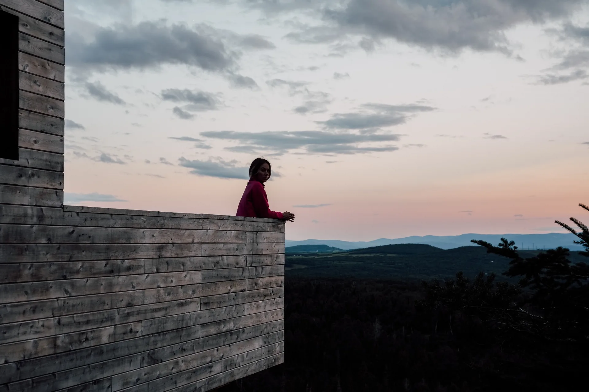 Personne accoudée à la terrasse en bois d'un refuge au crépuscule avec les montagnes de Charlevoix à l'horizon