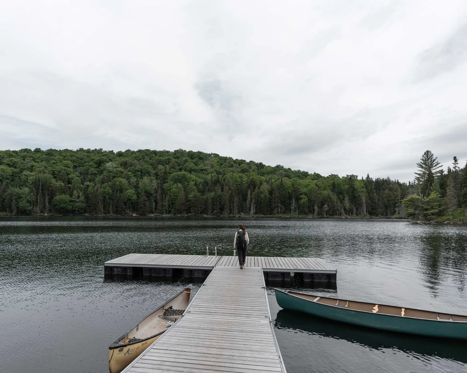 Person standing on a dock with canoes beside a forest lake, an idea for a nature getaway near Montreal