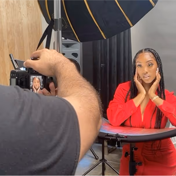 Behind-the-scenes shot of a professional photoshoot with a photographer taking a picture of a woman in a red outfit. 