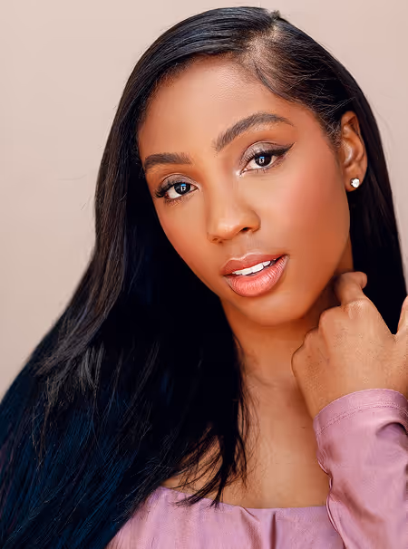 Headshot of a young woman with long, sleek dark hair and elegant makeup, wearing a lavender top. 