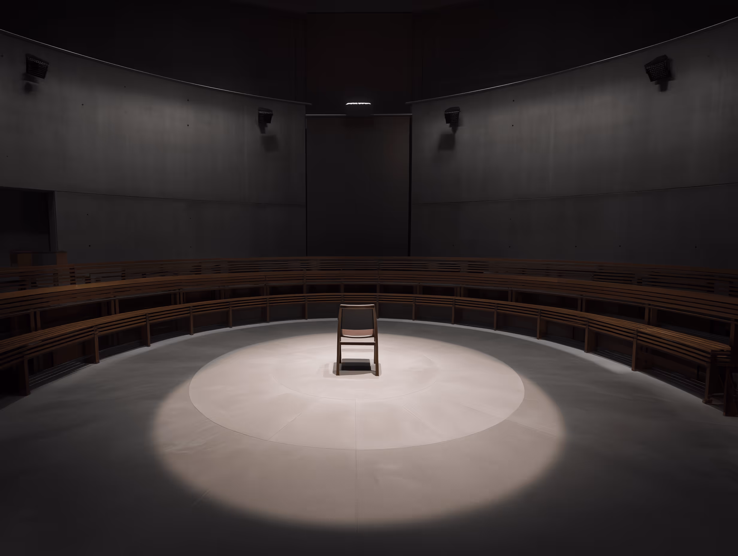 A single wooden chair illuminated by a spotlight in the center or a dark, empty auditorium with tiered seating.