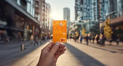 Una mano sostiene la tarjeta Mastercard Payphone y en el fondo se puede observar una ciudad.