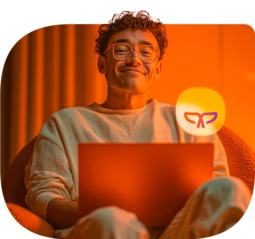 Hombre sonrie a la cárama mientras se encuentra con su laptop.