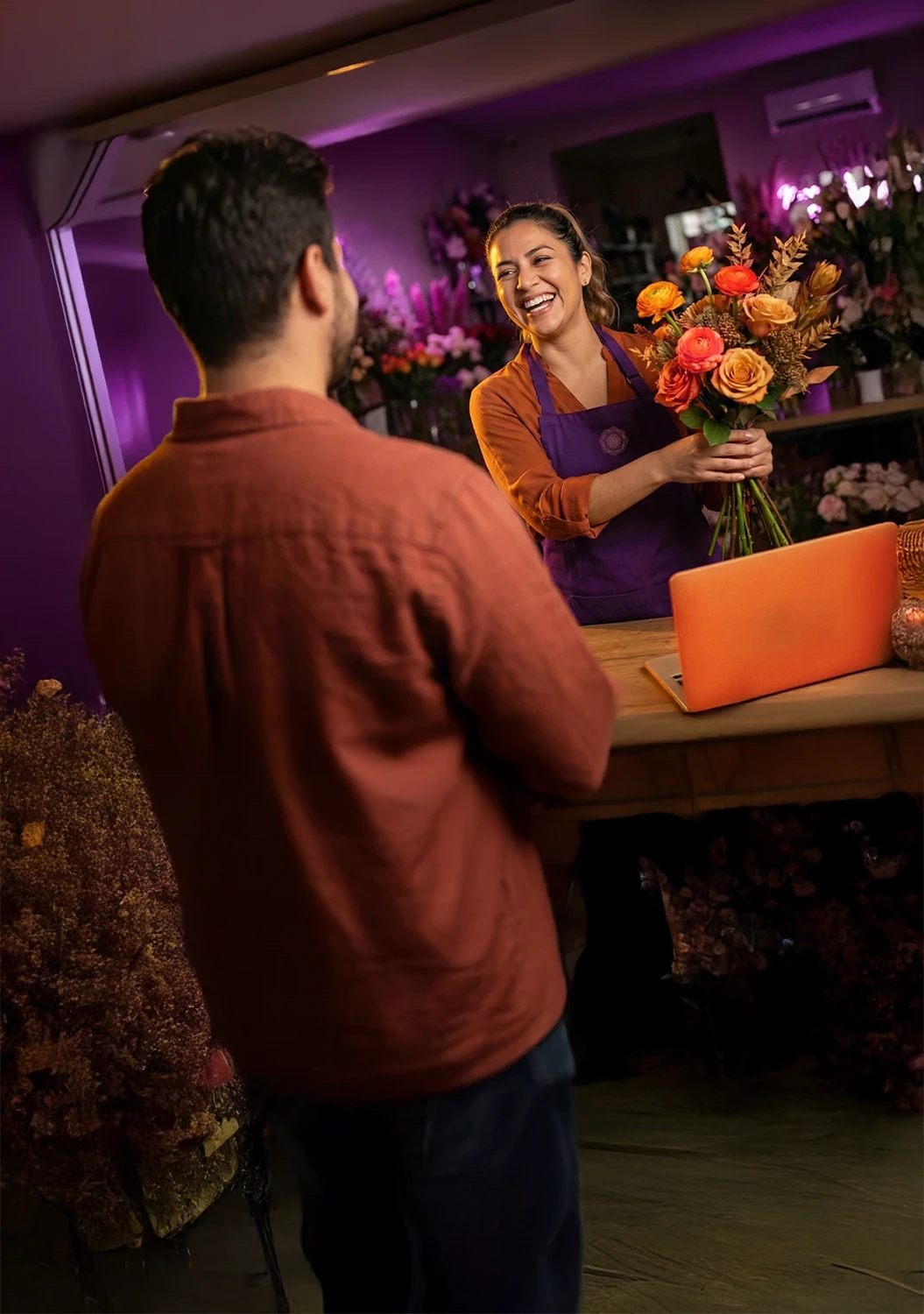 Emprendedora recibiendo flores de un hombre en el mostrador de su negocio.