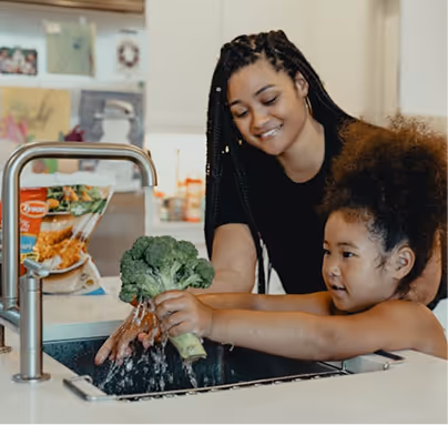 Mother and daughter washing fresh vegetables together in kitchen sink