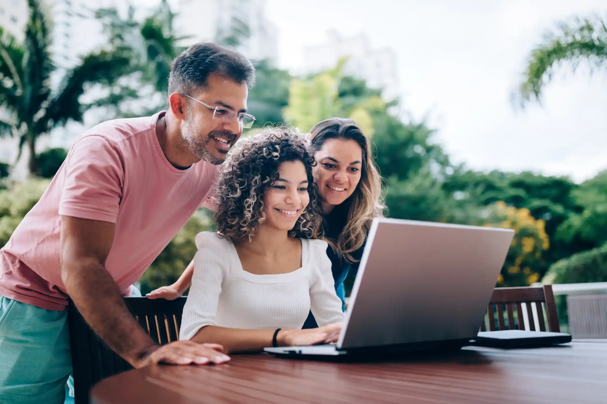 Three people smile together while working on laptop outdoors