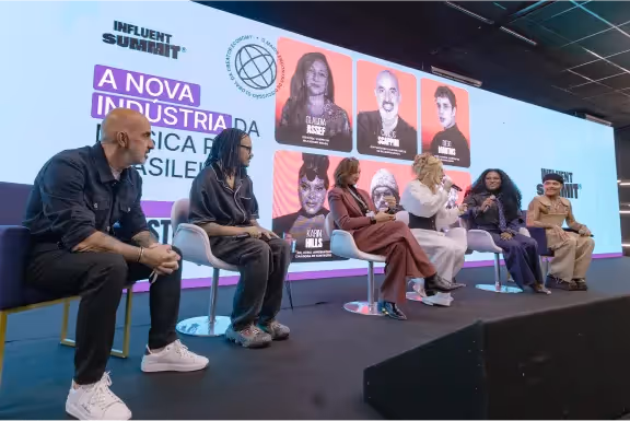 Painel com seis pessoas sentadas em cadeiras no palco durante o Influet Summit, com projeção ao fundo mostrando imagens e nomes dos palestrantes.