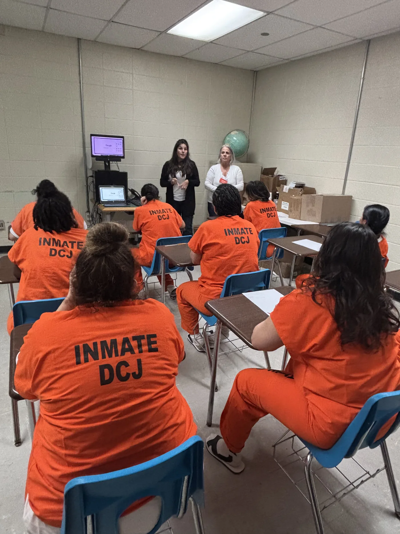 Students at desks in a Grow with Google digital skills class inside TGK jail in Miami, watching a Google demonstration on a monitor.