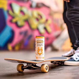 Perico Mimosa energy drink balanced on a skateboard with vibrant graffiti in the background, capturing youthful street style and clean energy. 