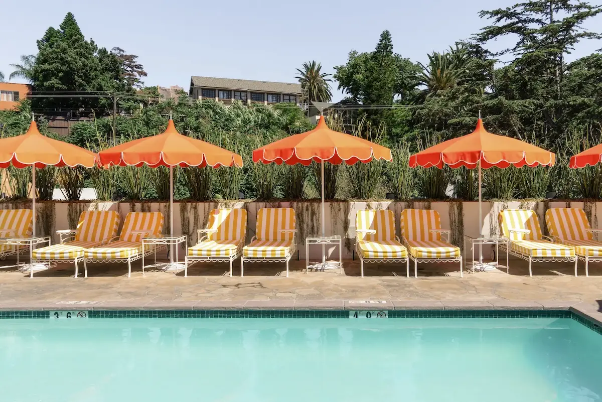 Outdoor pool with yellow-striped lounge chairs and orange umbrellas along the side under a clear sky.
