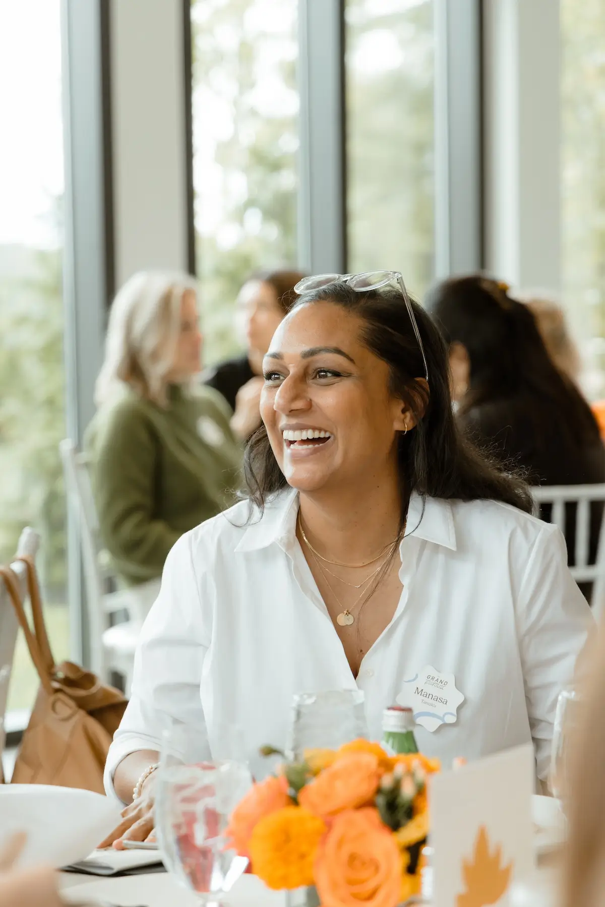 Smiling woman in white shirt with name tag sitting at a table with orange flowers in the foreground.