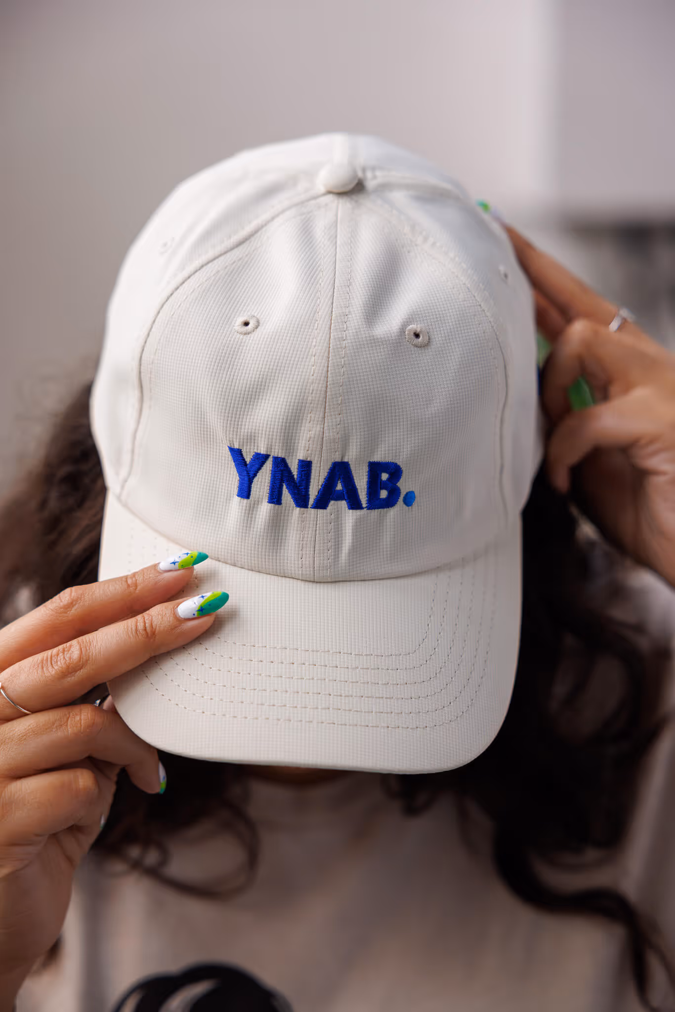 Person wearing a beige cap with 'YNAB.' embroidered in blue, partially covering their face.