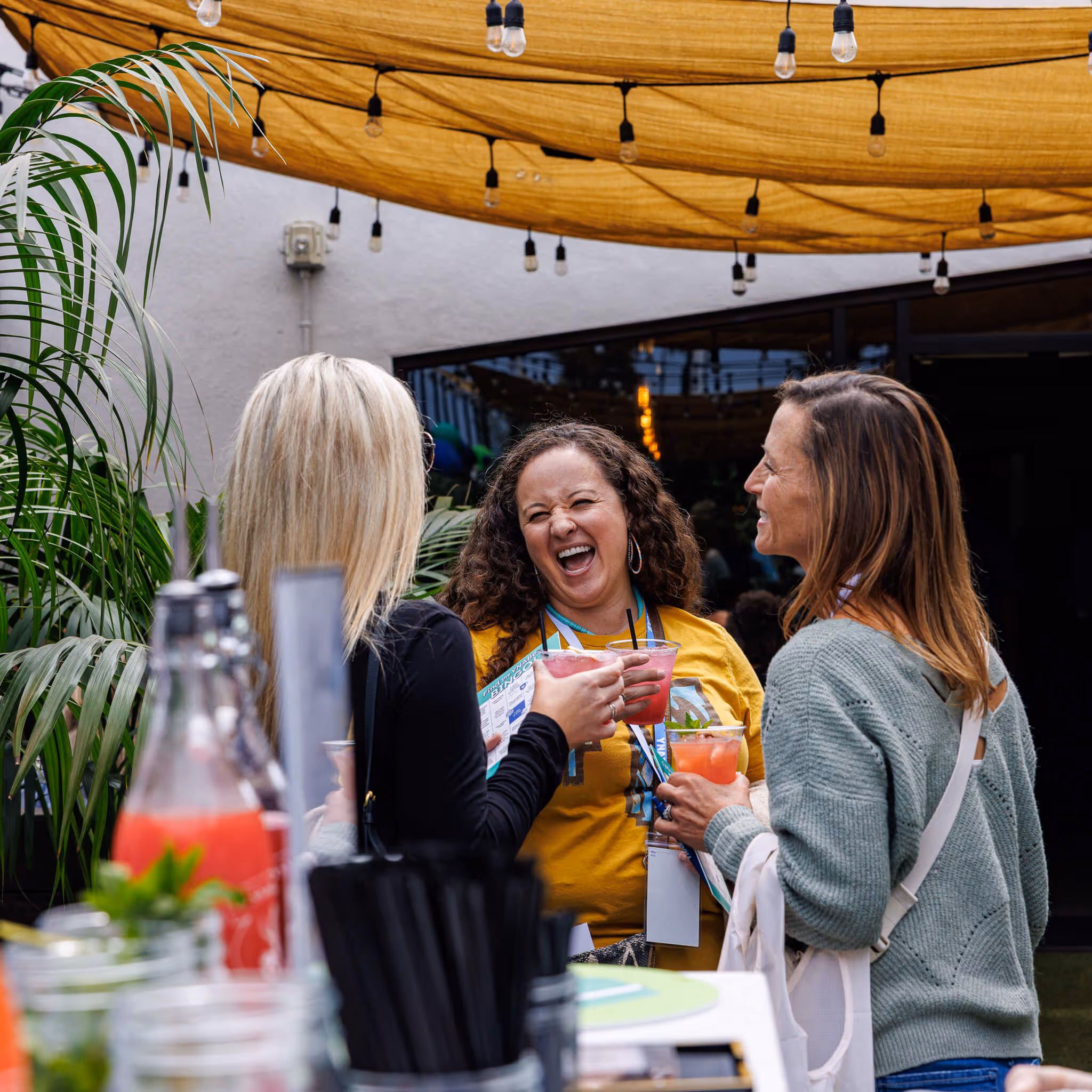 Group of people laughing and chatting at an outdoor table under string lights.