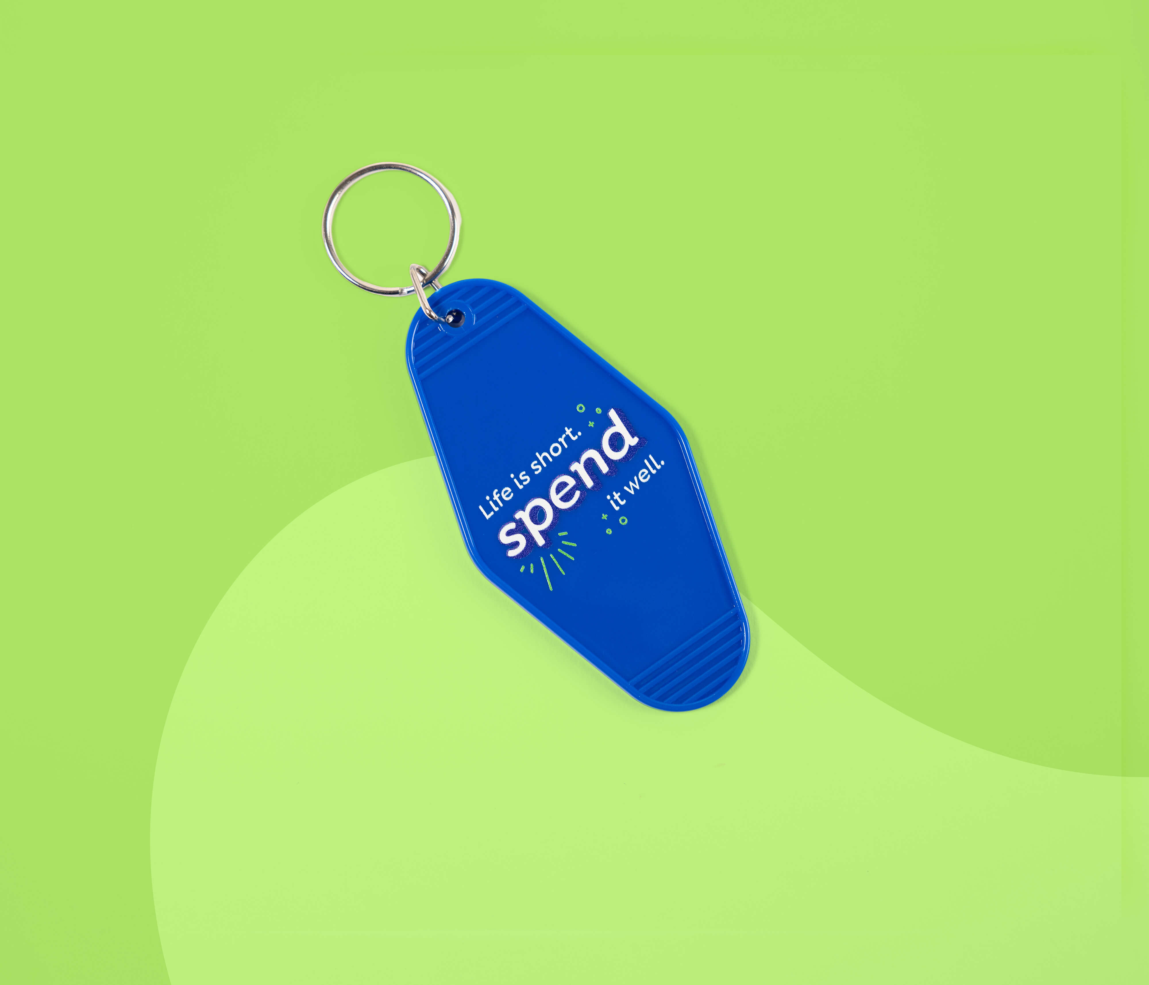 Blue YNAB keychain reading “Life is short. spend it well.” on a green background.