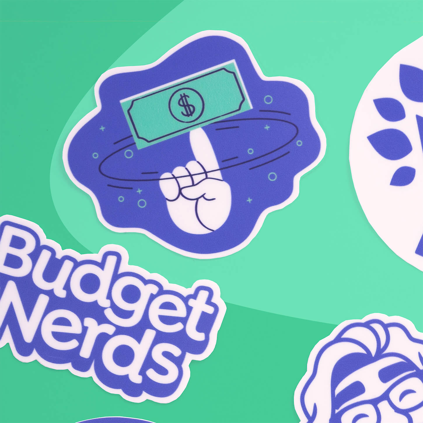 YNAB vinyl sticker showing a hand spinning a dollar bill on one finger, surrounded by other stickers on a teal background.