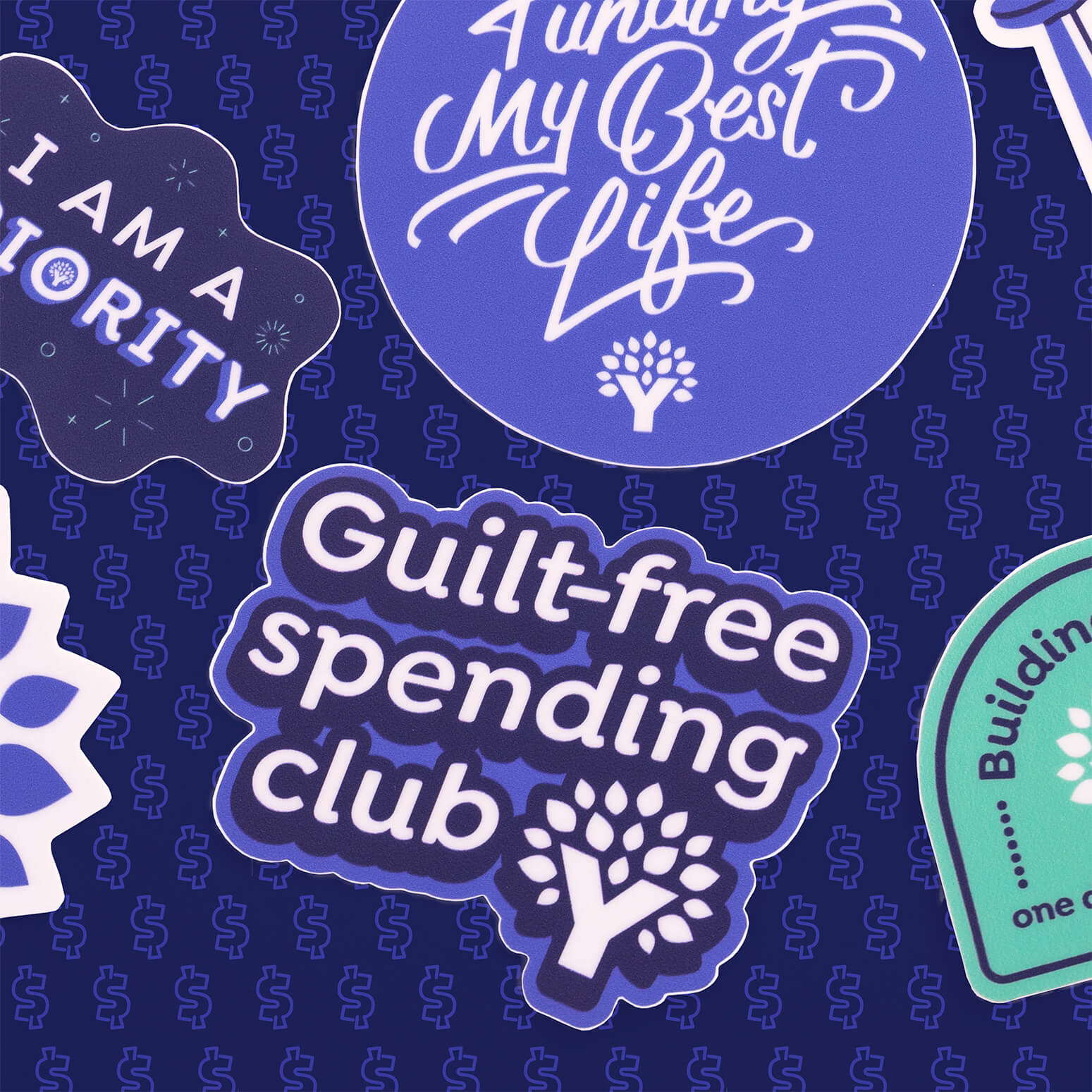 Vinyl YNAB sticker reading “Guilt-free spending club” on dark patterned background with other YNAB stickers.