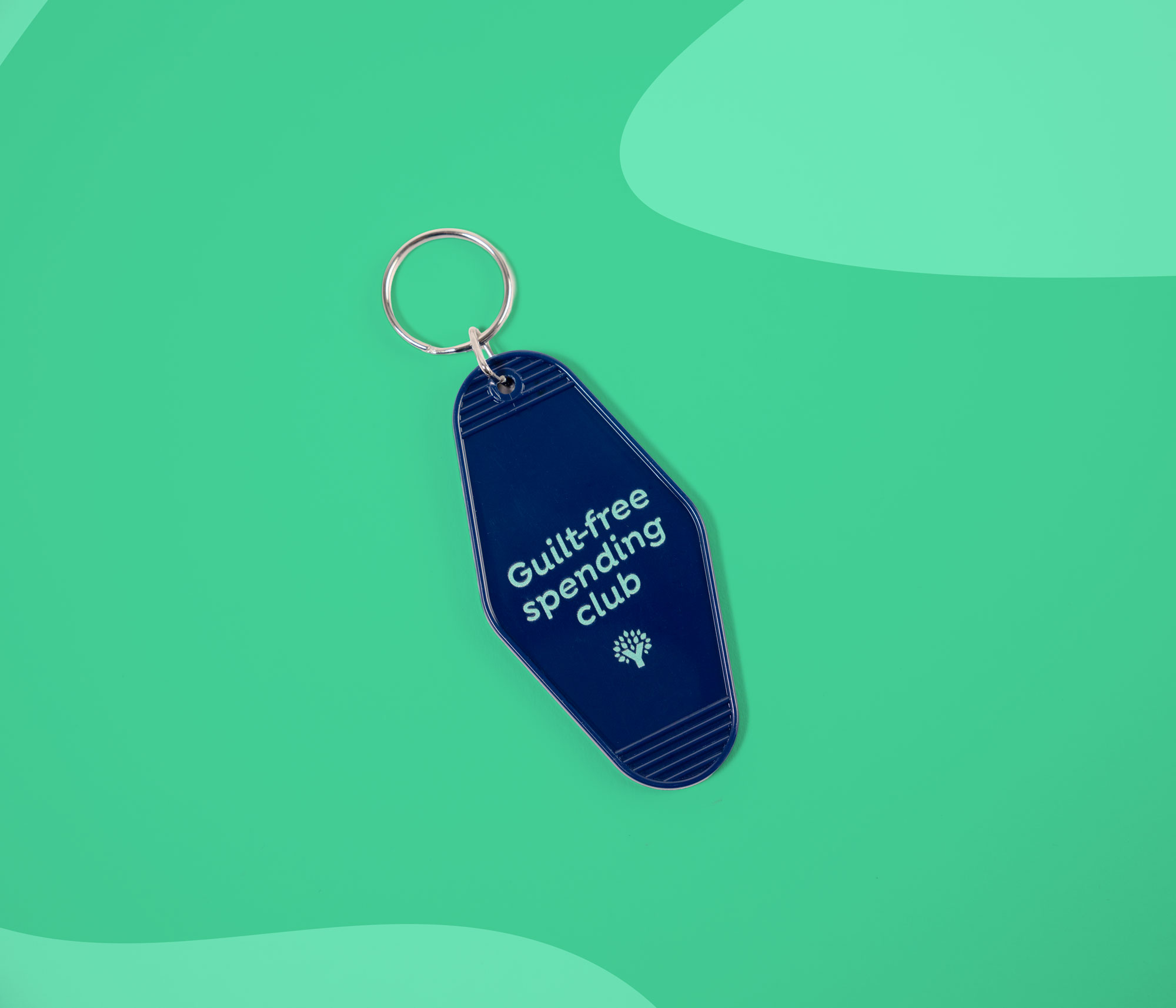 Navy keychain reading “Guilt-free spending club” on a teal background.