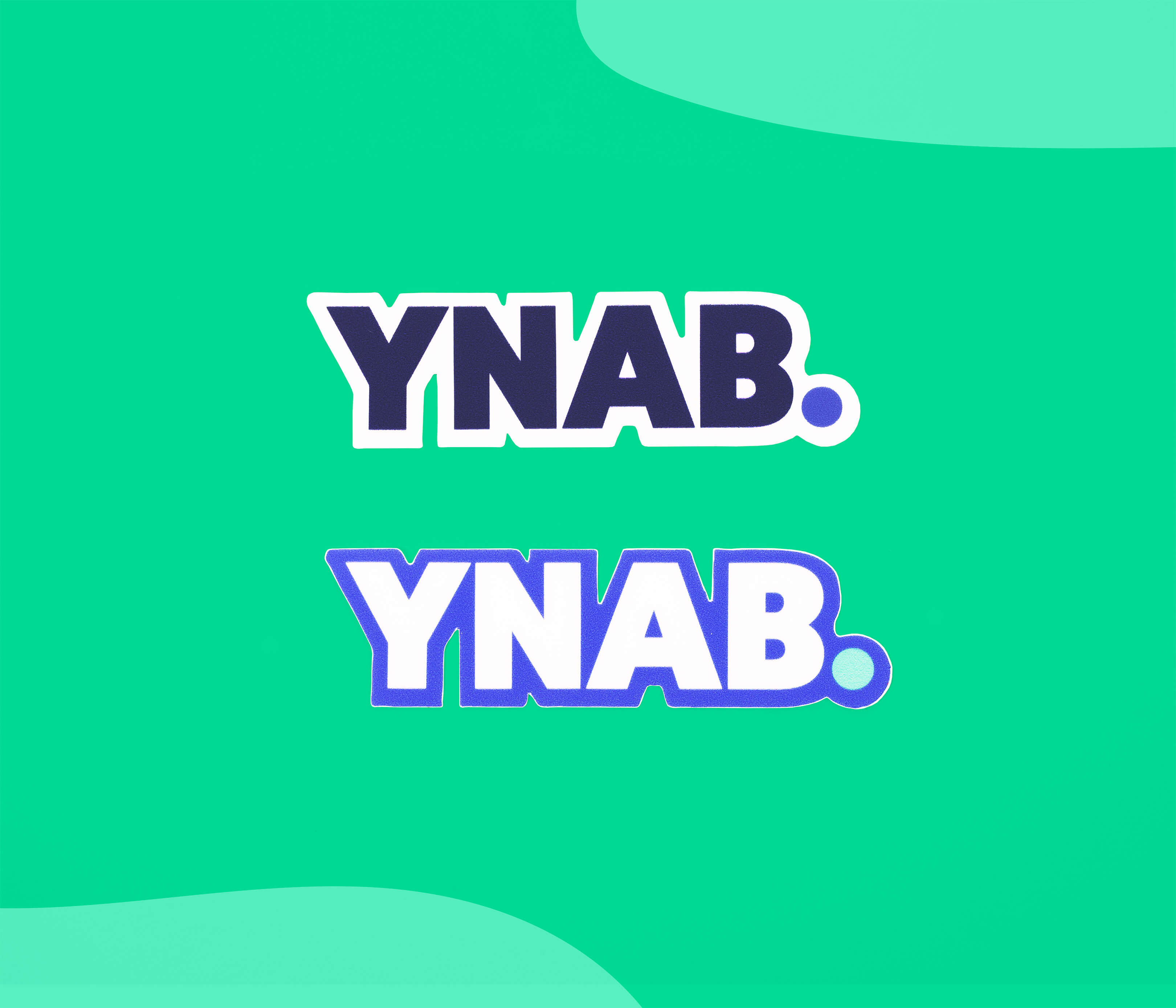 Two YNAB logo stickers—one dark blue with a white outline and one white with a blurple outline—displayed on a teal background.