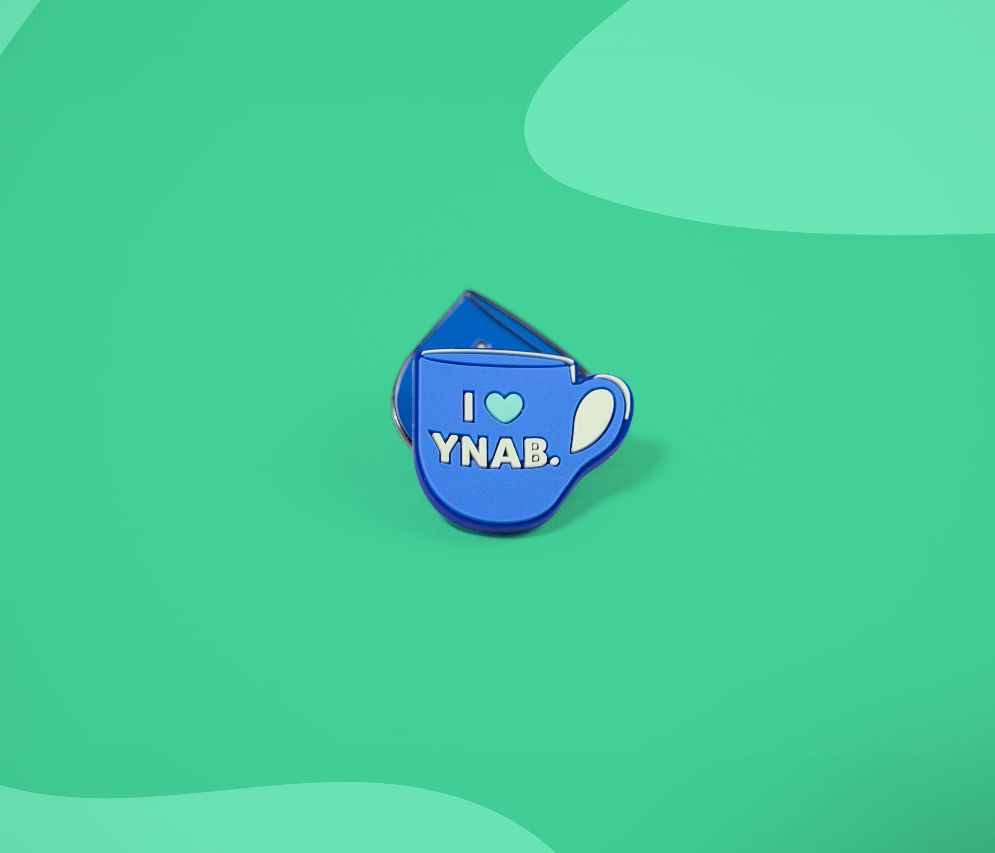 Two blue mug-shaped Croc charms with the text "I love YNAB." stacked slightly on a teal background.