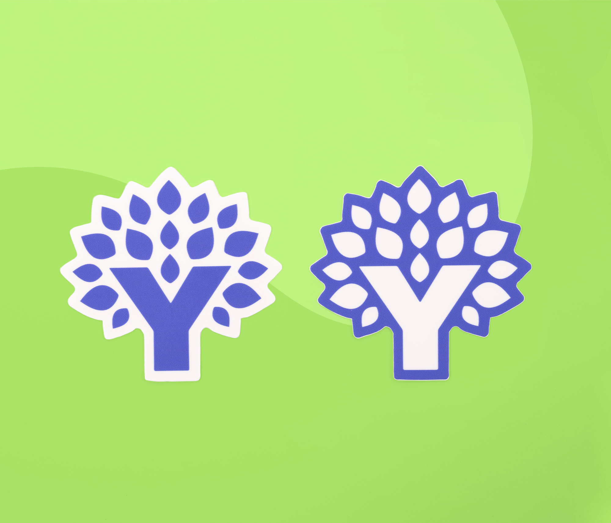 Two diecut YNAB Tree stickers, one with a white border and one with a blue border, on a green background.