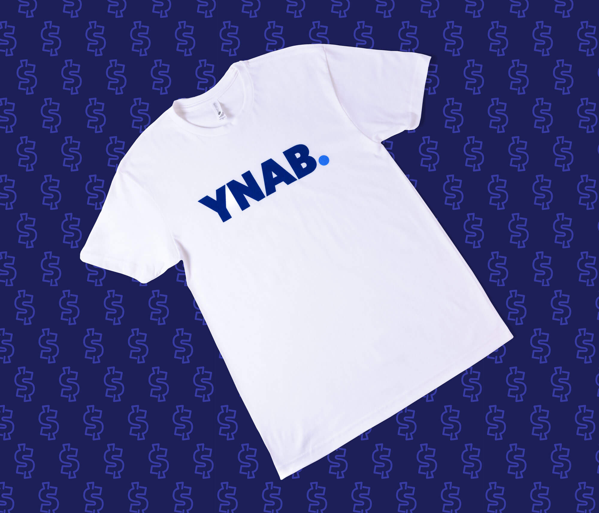 White YNAB t-shirt with bold blue logo displayed on a navy patterned background.