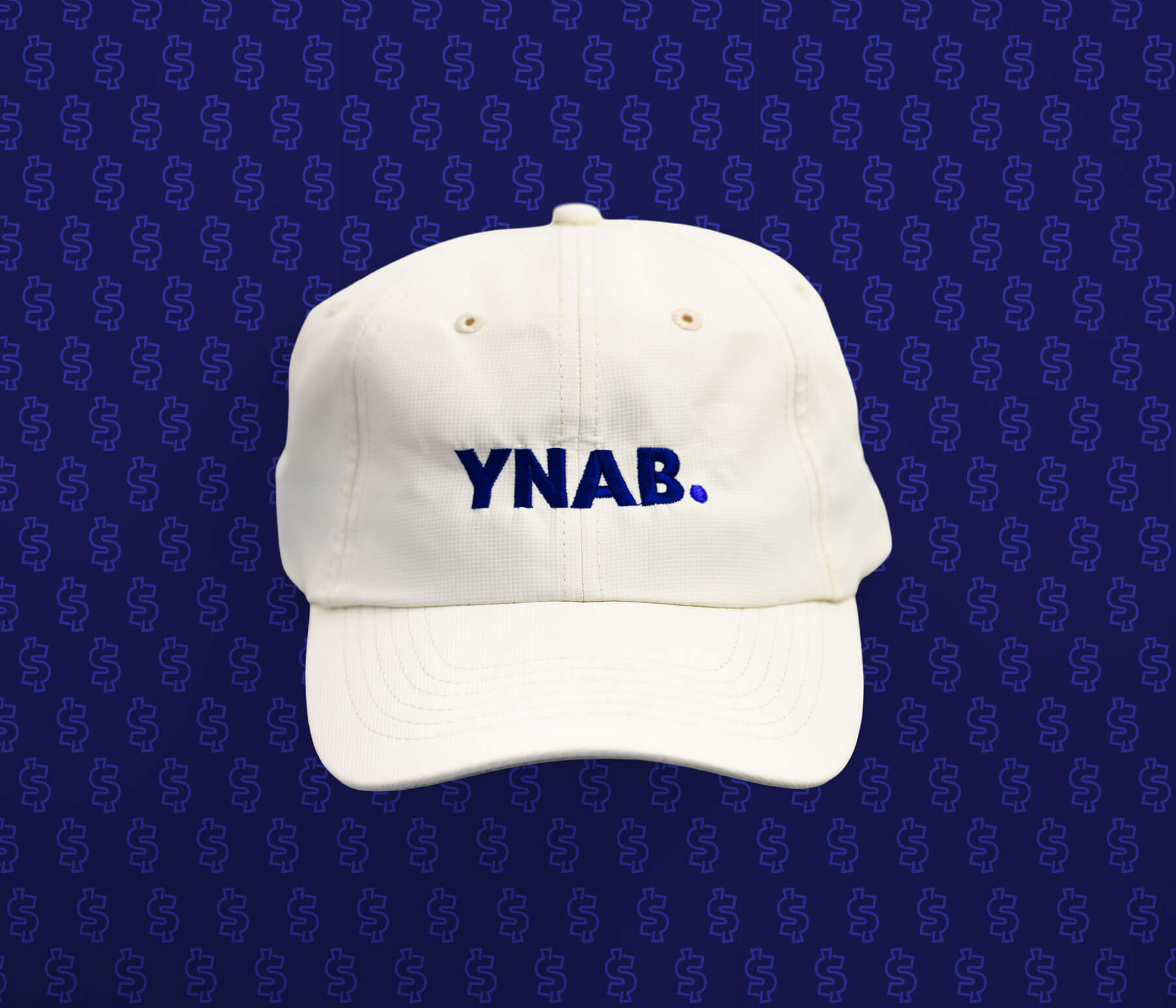 Cream YNAB hat with blue embroidered logo, displayed on a dark navy background.